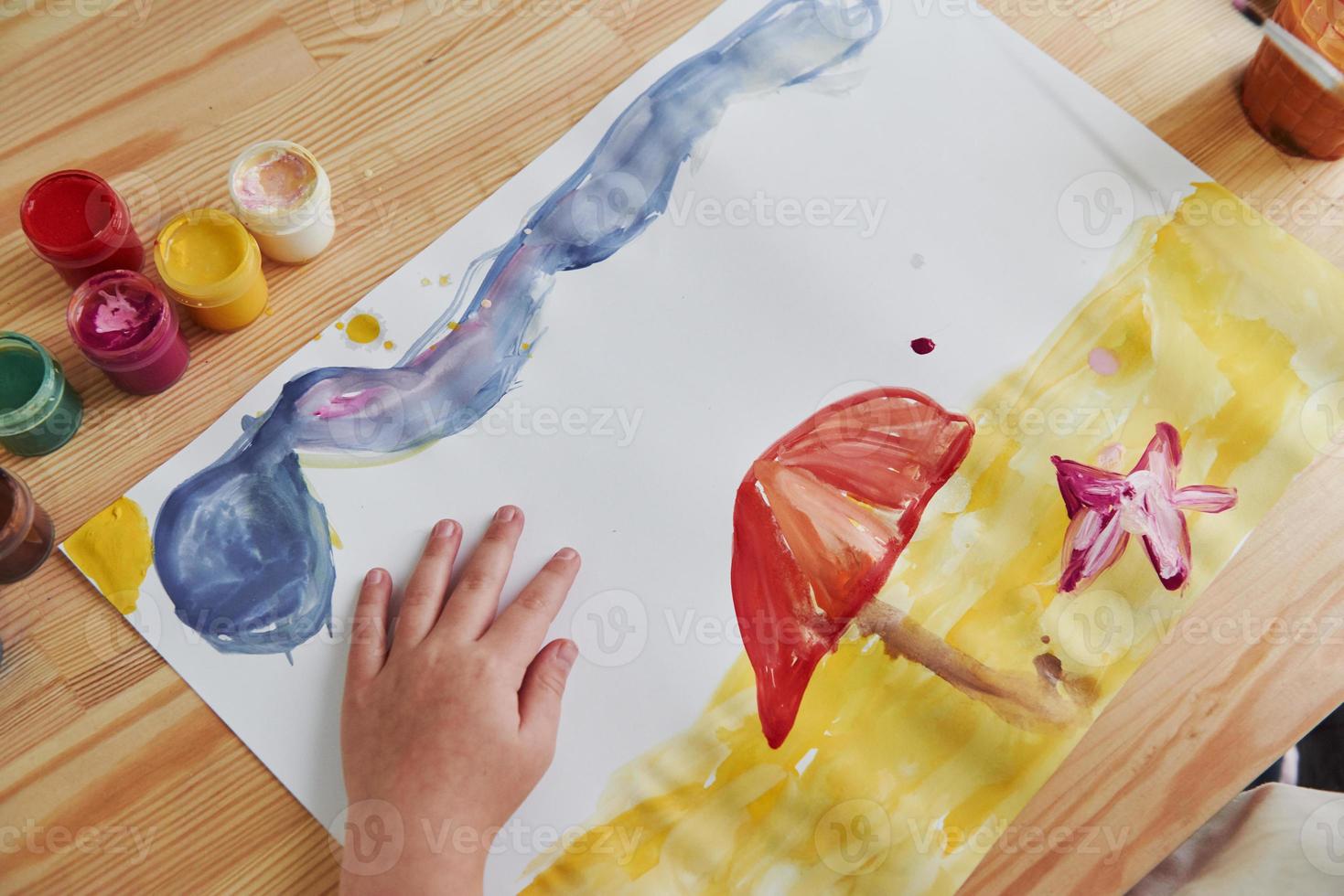 Picture of beach with sand, star and clouds. Little girl is drawing by using gouache and brush. Learning in the art class photo