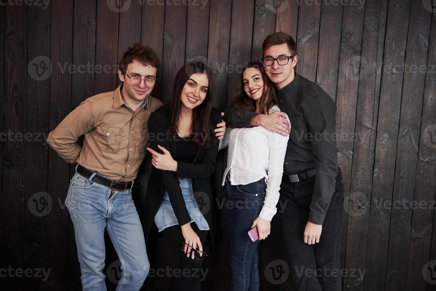 jóvenes satisfechos. el joven se para contra la pared de madera negra. grupo de amigos pasando tiempo juntos foto