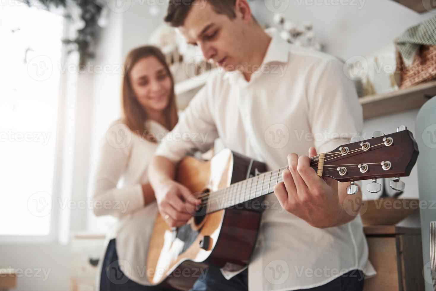 marido concentrado. joven guitarrista tocando una canción de amor para su novia en la cocina foto