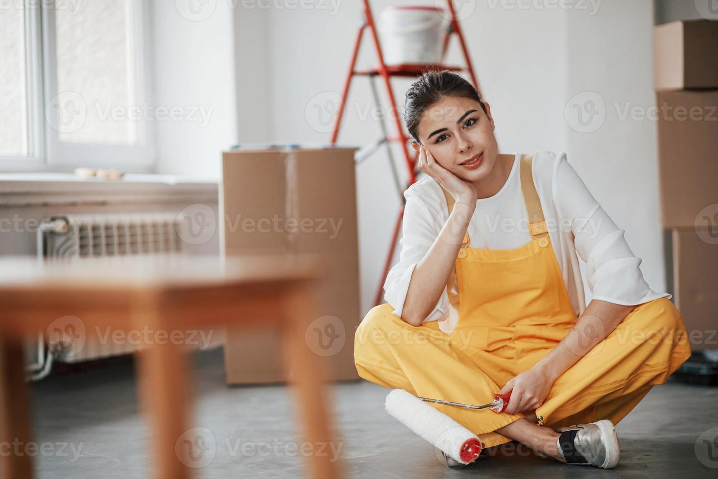 Attractive female worker sitting in front of red ladder. Young brunette in the room with white walls and daylight that comes from the window photo