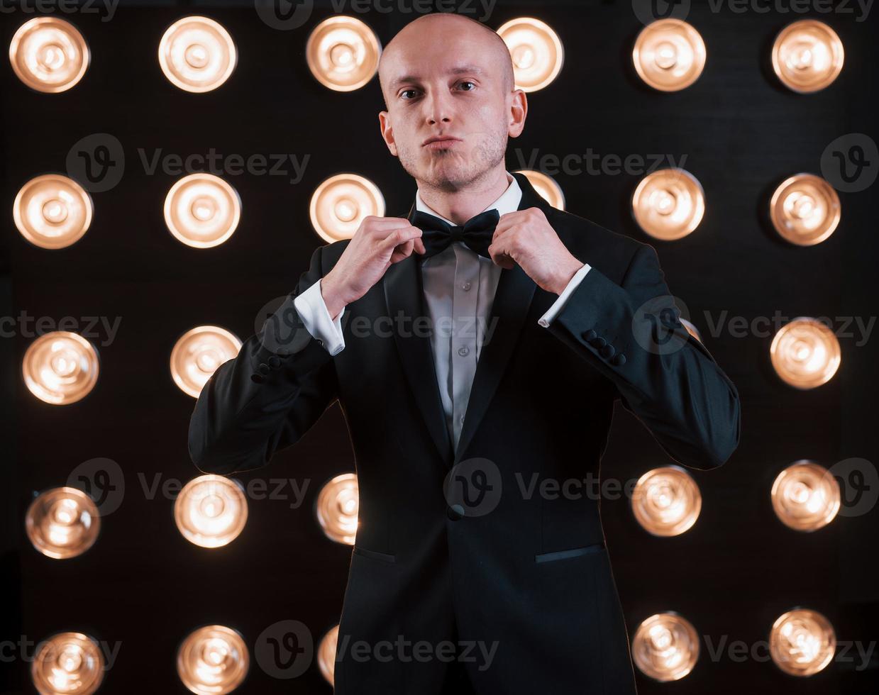 Adjusts the tie. Ready for the show. Magician in black suit standing in the room with special lighting at backstage photo