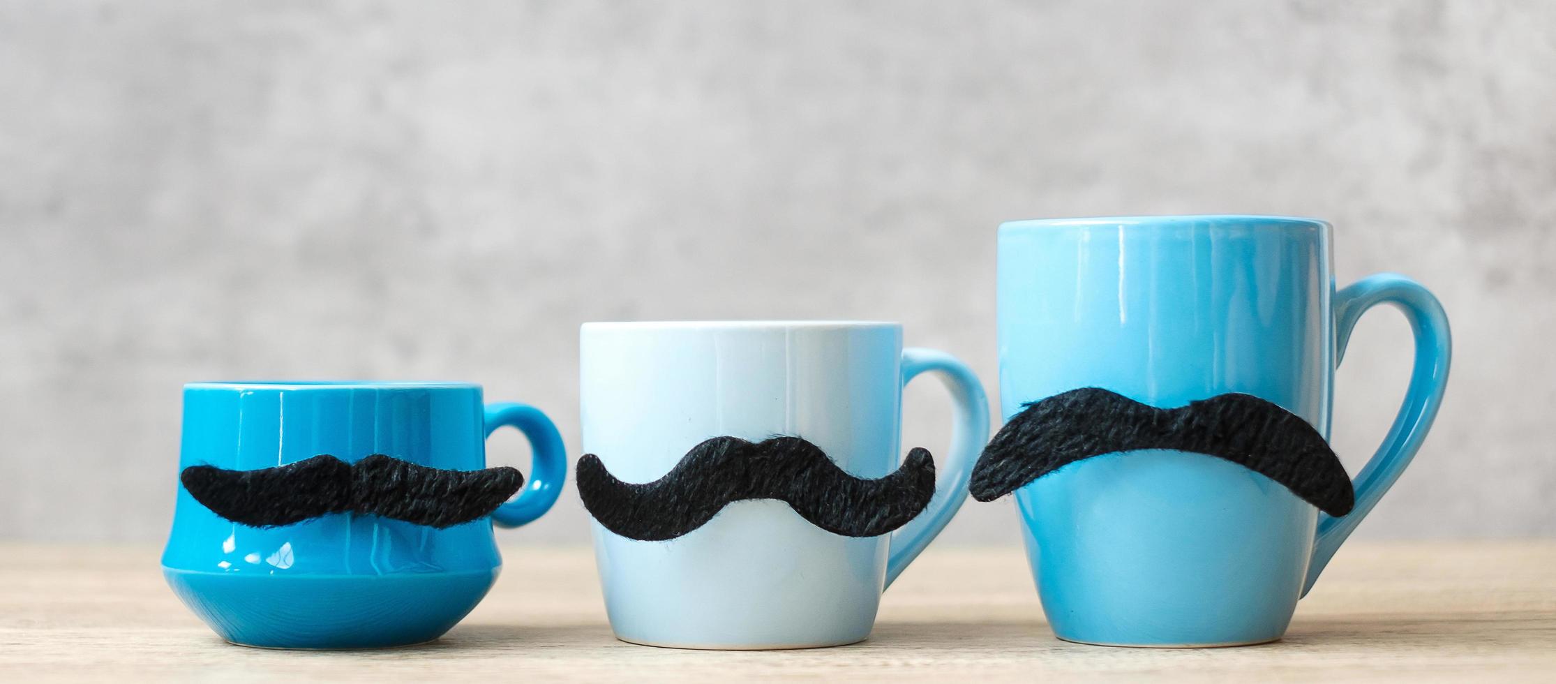 Blue coffee cup and tea mug with Black mustache decor on wood table background in the morning. Blue November, Happy Father day and International men day concept photo