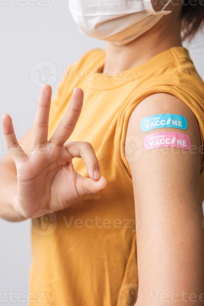 woman showing OK sign with bandage after receiving covid 19 vaccine. Vaccination, herd immunity, side effect, booster dose, vaccine passport and Coronavirus pandemic photo