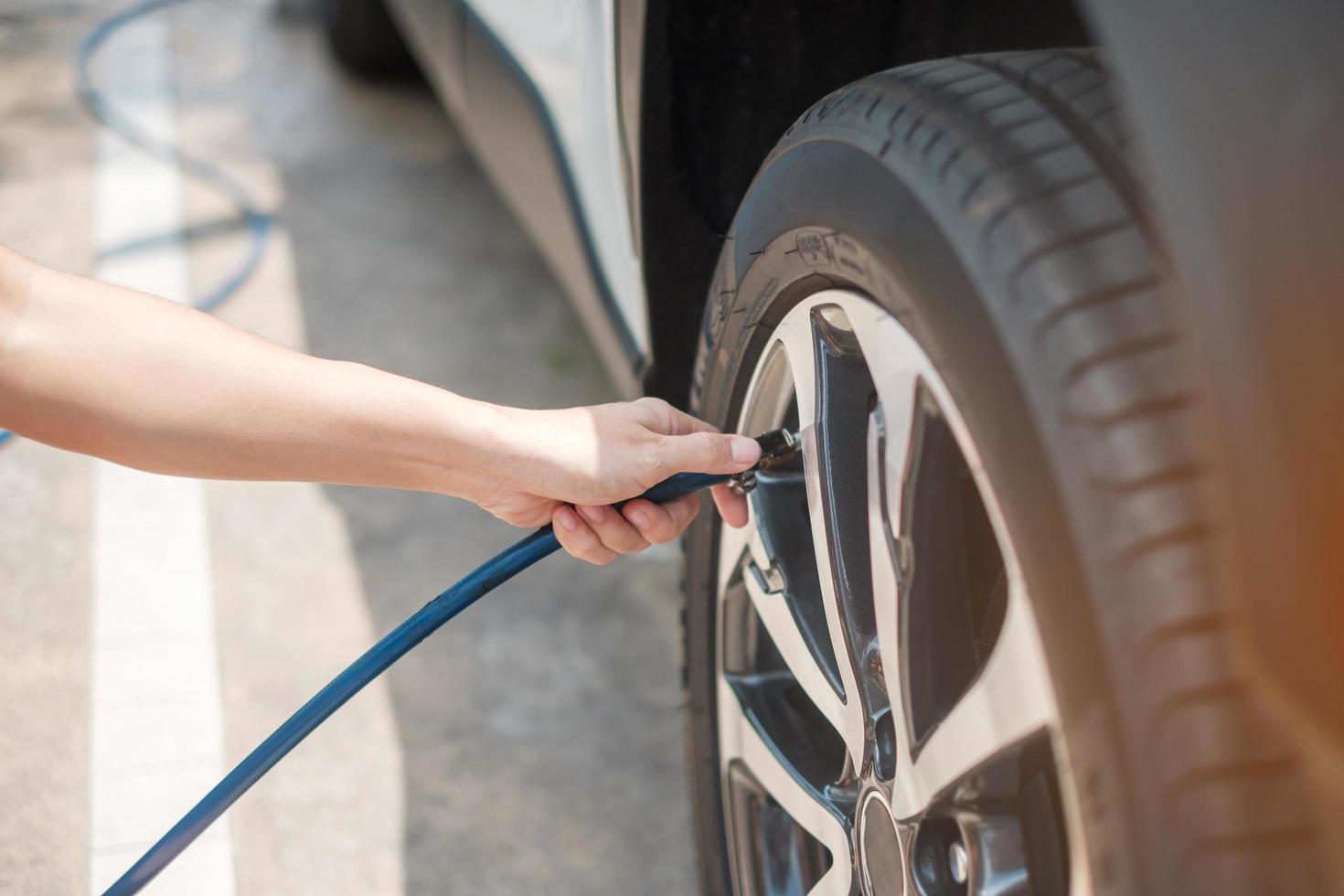 hand inflating tires of vehicle, checking air pressure and filling air on car wheel at gas station. self service, maintenance and safety transportation concept photo