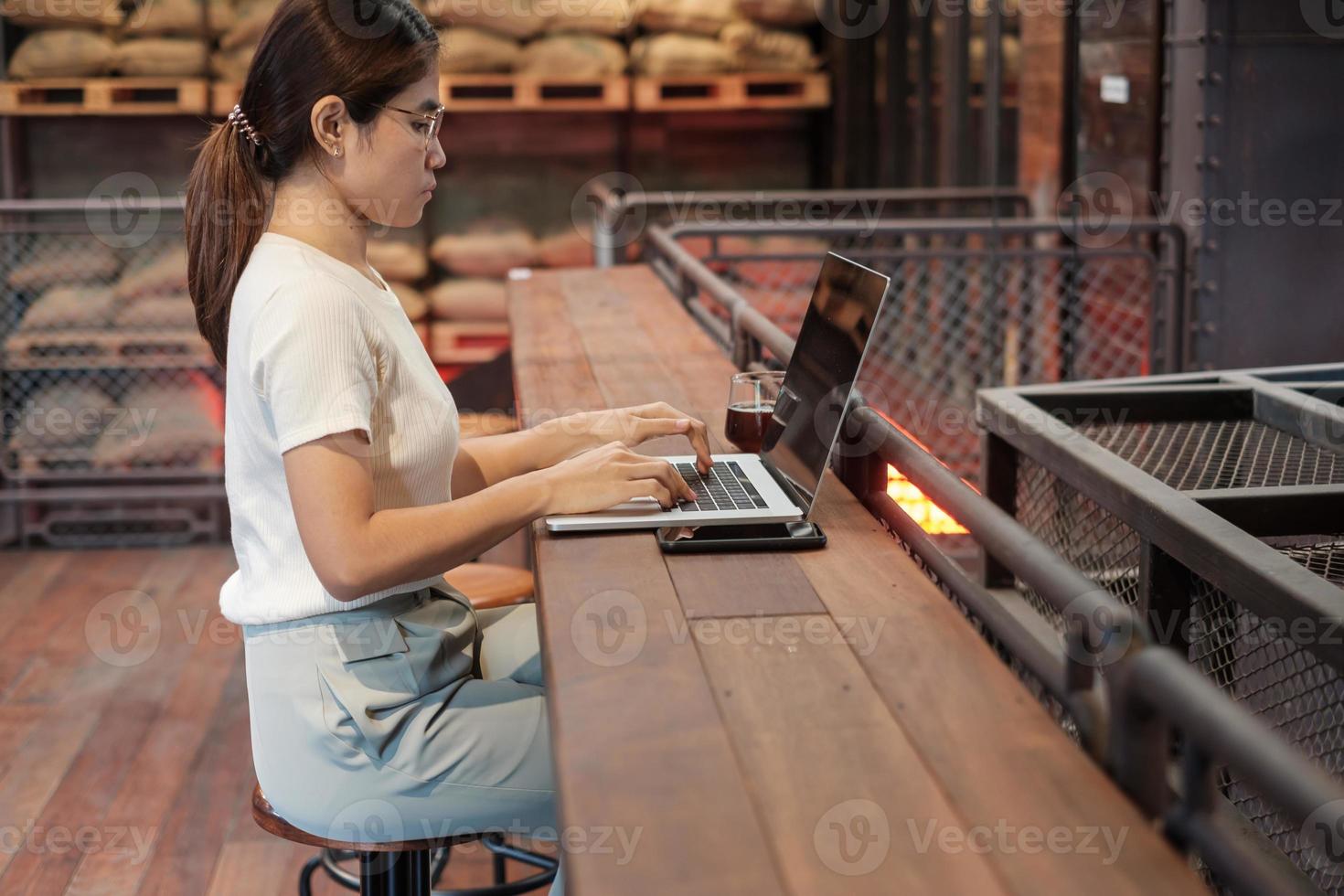 mujer de negocios informal que usa un teléfono inteligente y una computadora portátil, una mujer independiente que escribe un teclado en una cafetería o en una oficina moderna. tecnología, concepto digital en línea y de red foto