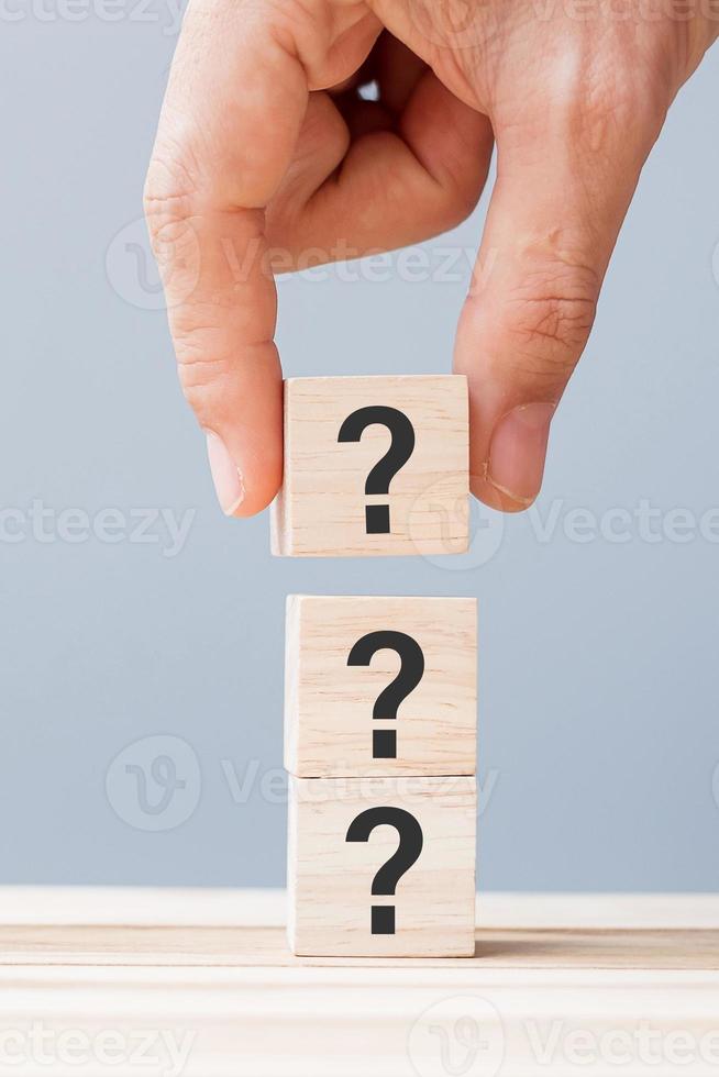 hand holding Questions Mark on wooden cube block on table background. FAQ, Answer, Q and A, Information, Communication and interrogation Concepts photo