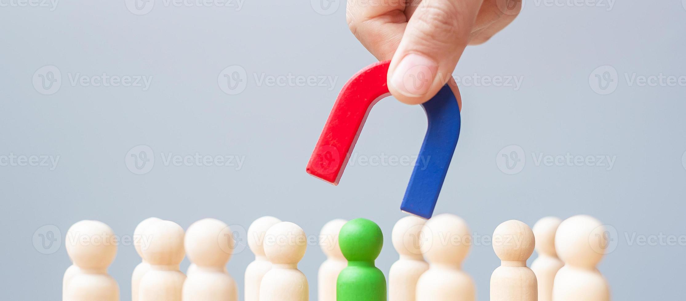 Business man hand holding magnet and pulling man wooden figure from the crowd employee. Business, Human resource management, Recruitment, Teamwork, strategy, toxic people and leadership Concepts photo