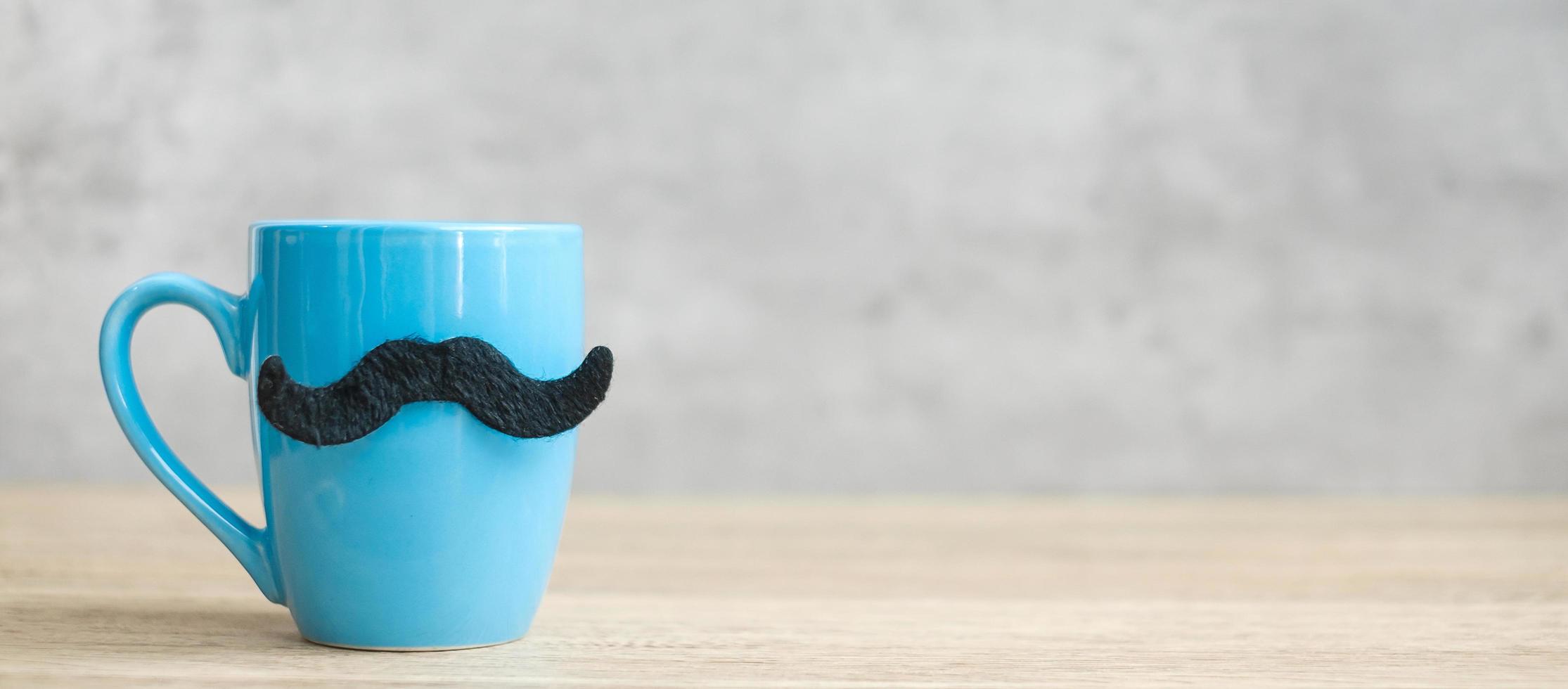 Blue coffee cup or tea mug with Black mustache decor on table. Blank copy space for text. Blue November, Happy Father day and International men day concept photo