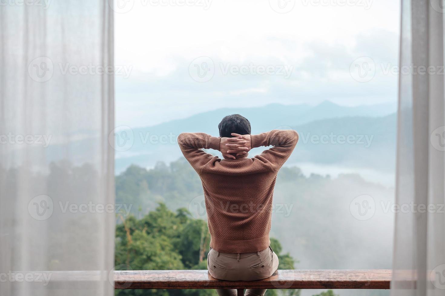 happy tourist man relaxing and looking mountain view at countryside home or homestay in the morning. Vacation, blogger, SoloTravel, journey, trip and relaxing concept photo