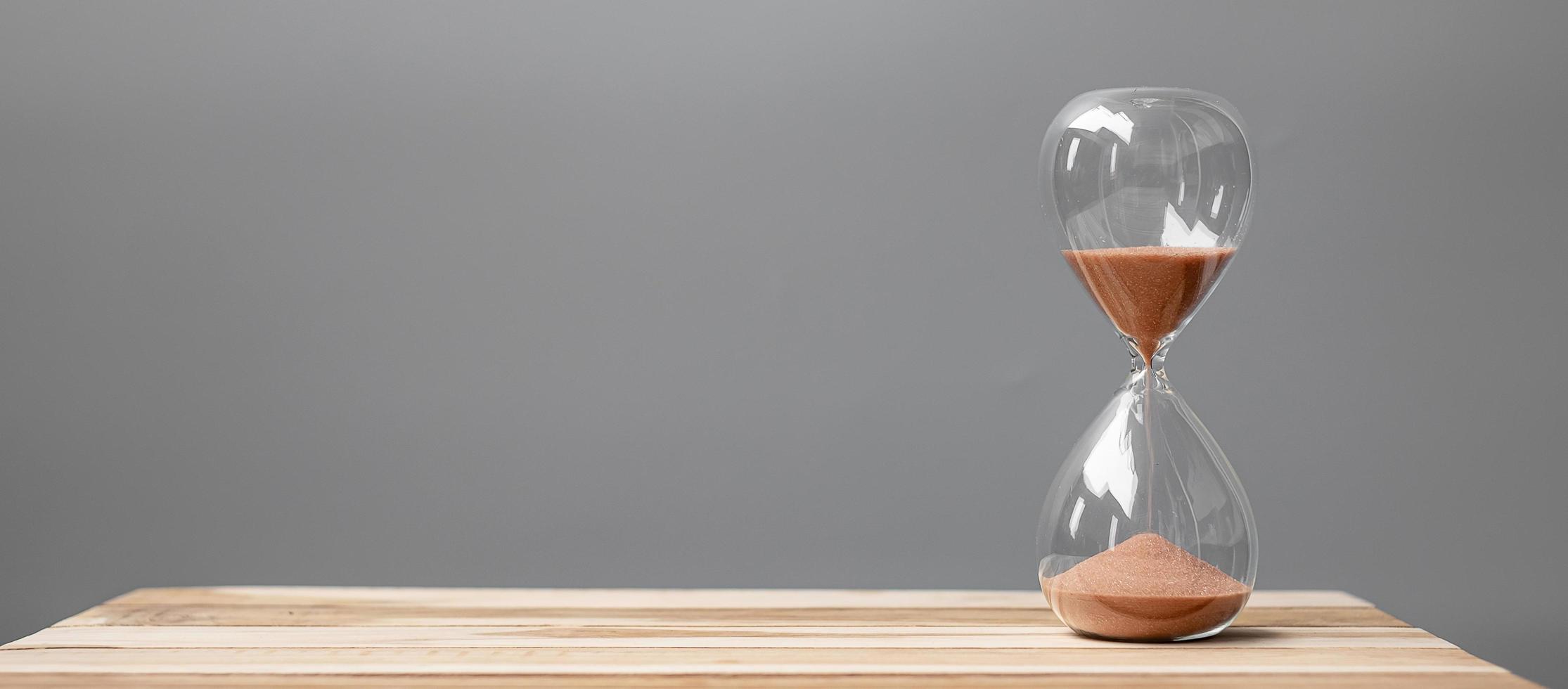 reloj de arena en la oficina de mesa con espacio para copiar, arena que fluye a través de la bombilla de reloj de arena que mide el tiempo que pasa. cuenta regresiva, fecha límite, tiempo de vida y concepto de jubilación foto