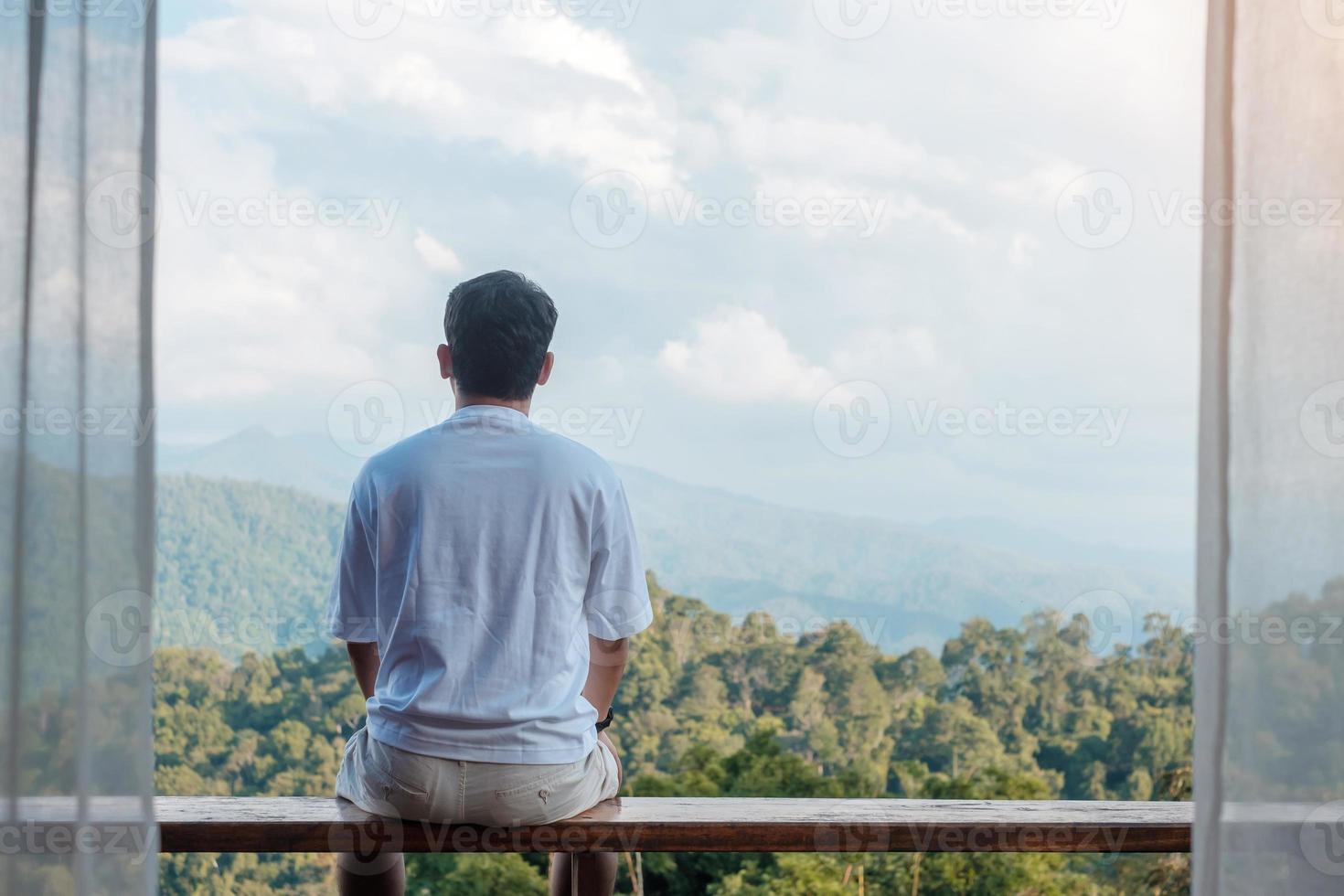 Happy tourist man relaxing and looking mountain view at countryside home or homestay in the morning. Vacation, blogger, SoloTravel, journey, trip and relaxing concept photo
