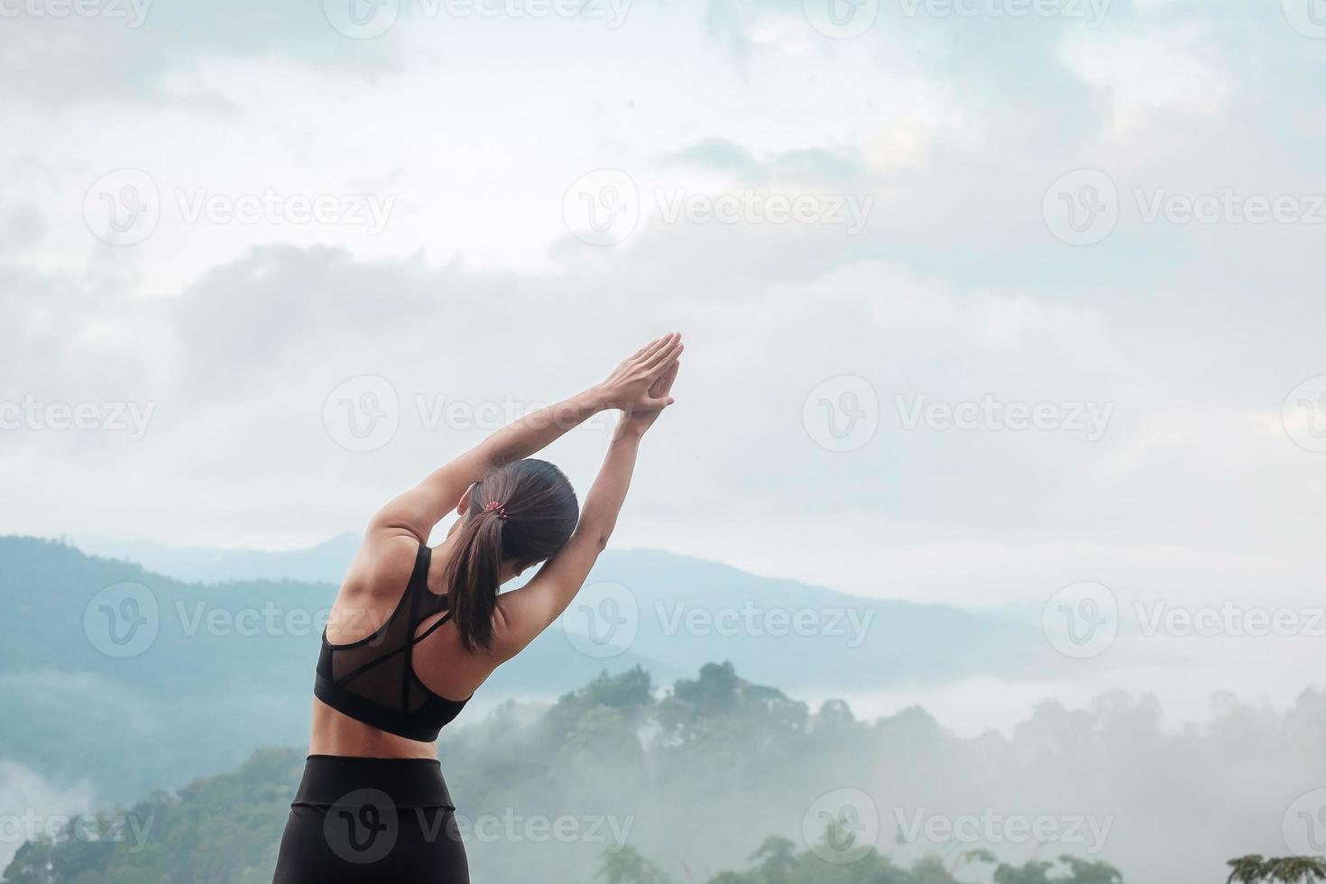 mujer joven haciendo yoga y estirando los músculos por la mañana, meditación de niña sana contra la vista a la montaña. conceptos de bienestar, fitness, vitalidad, ejercicio y equilibrio entre la vida laboral y personal foto