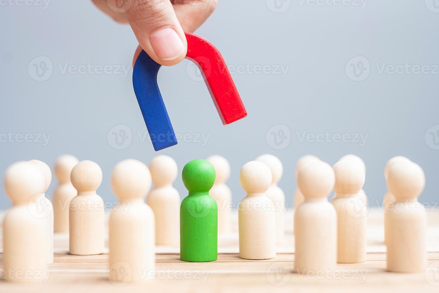 Business man hand holding magnet and pulling man wooden figure from the crowd employee. Business, Human resource management, Recruitment, Teamwork, strategy, toxic people and leadership Concepts photo