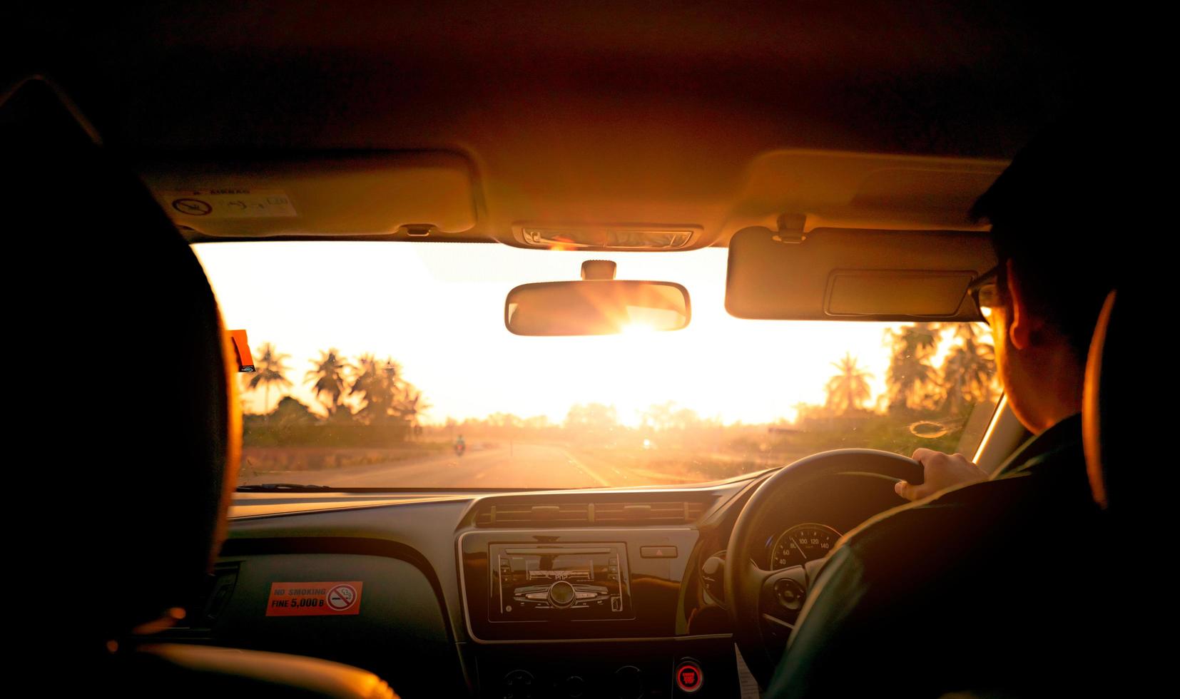 Back view of a man driving car for summer road trip travel. Car driving with safety on asphalt road. Driver hand holding steering wheel for control car. Inside view of car. Dashboard and windshield. photo