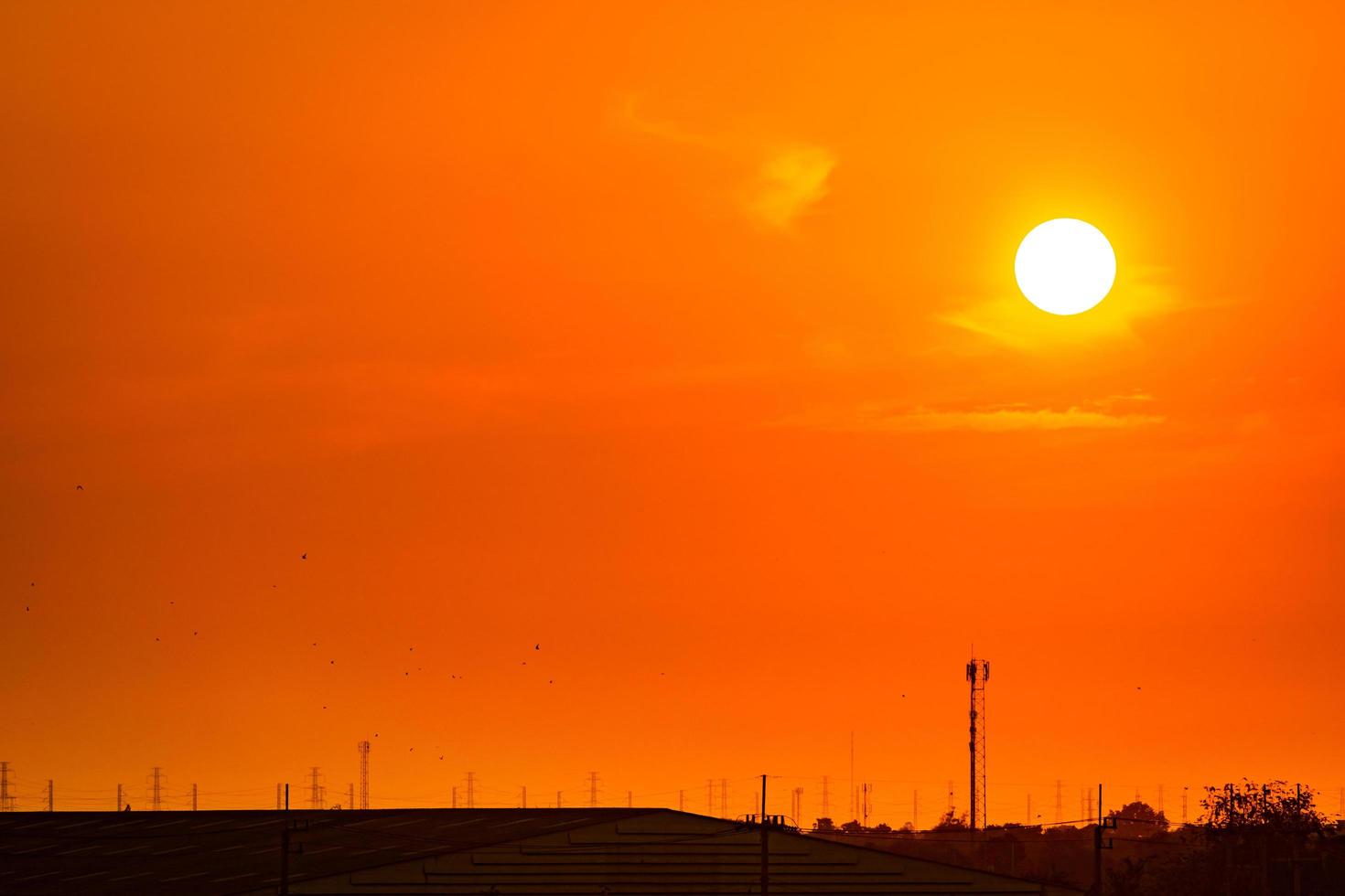 Beautiful orange sunset sky with roof of factory and birds flying near high voltage electric pylons. Evening sunset sky at industrial zone. Power and energy concept. High voltage grid tower. photo