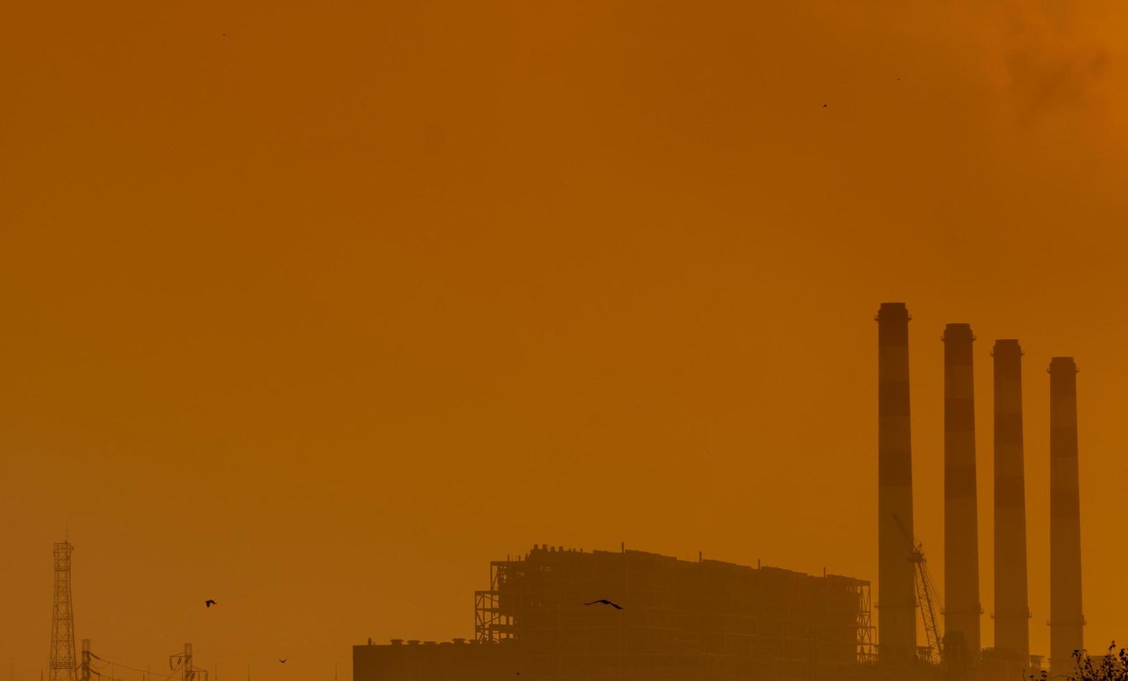 Power plant with orange sunset sky and birds flying on the sky. Air pollution concept. Energy for support factory in industrial estate. Power and energy. Dust spread in the air in the evening. photo