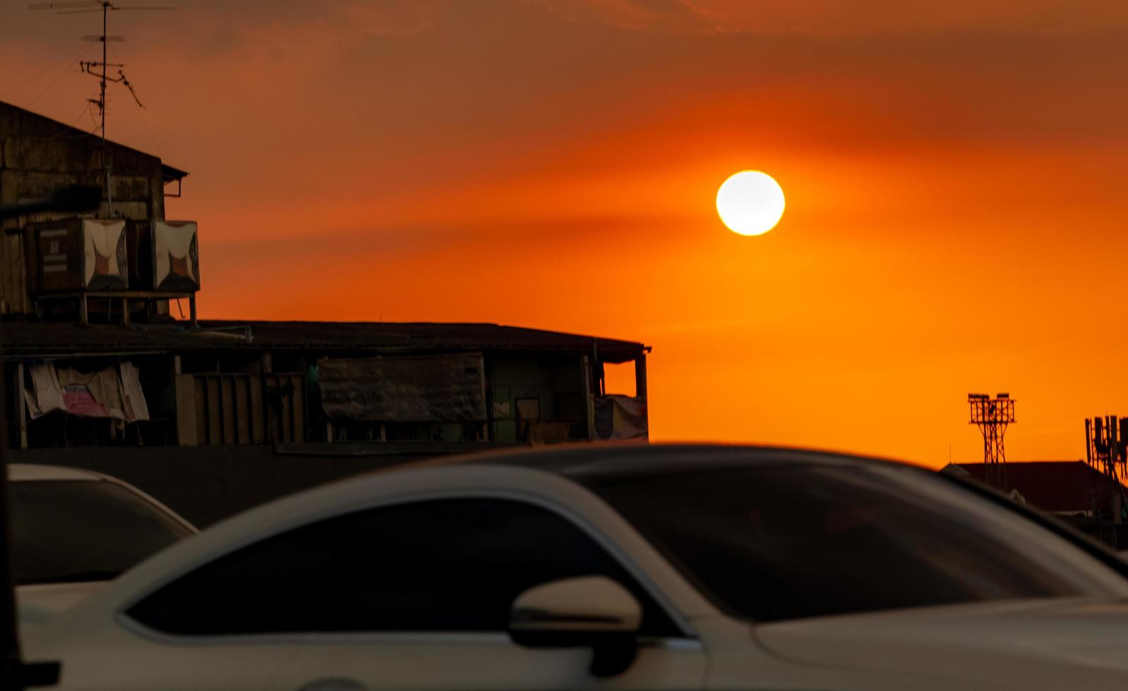 Blurred white Car driving on the road near slum community at sunset with beautiful orange sunset sky. Traffic jam in town while sunset in the evening. Beautiful view or great moment in rush hours. photo