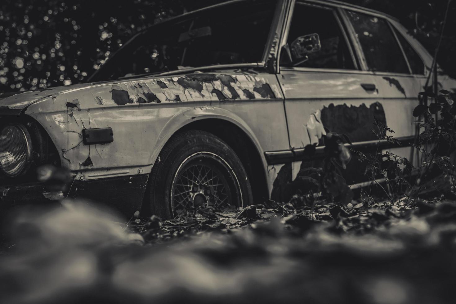 viejo coche destrozado en escena en blanco y negro. coche oxidado abandonado en el bosque sobre fondo bokeh. coche abandonado destrozado y oxidado. el arte del auto usado abandonado. tragedia y pérdida. tristeza foto