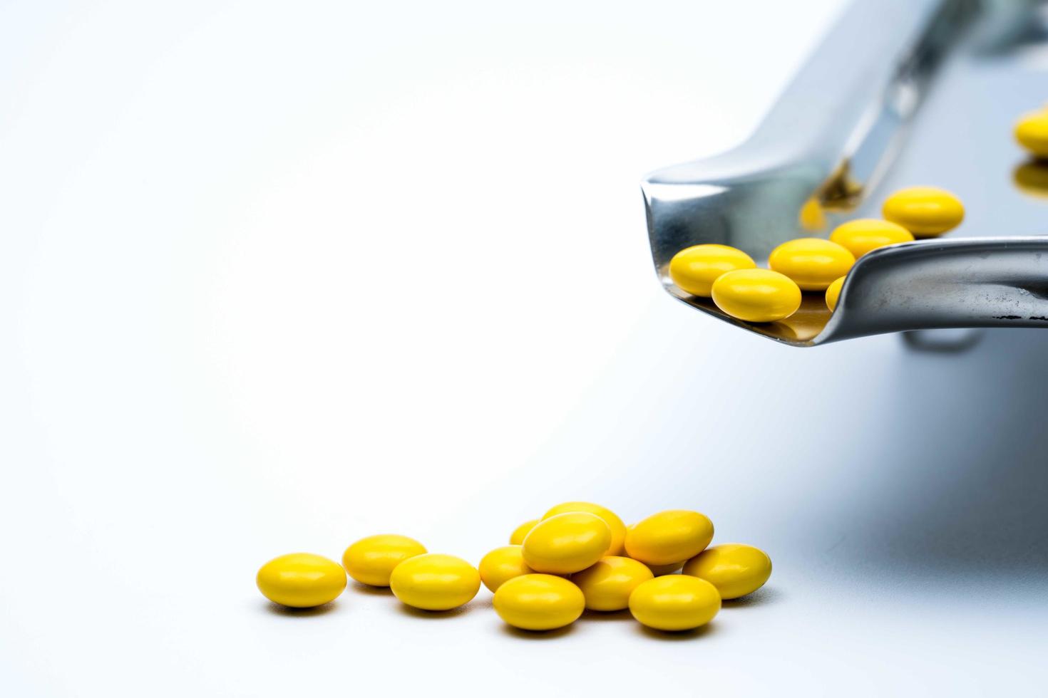 Macro shot detail of yellow round sugar coated tablets pills on stainless steel drug tray and some of them are on white background photo