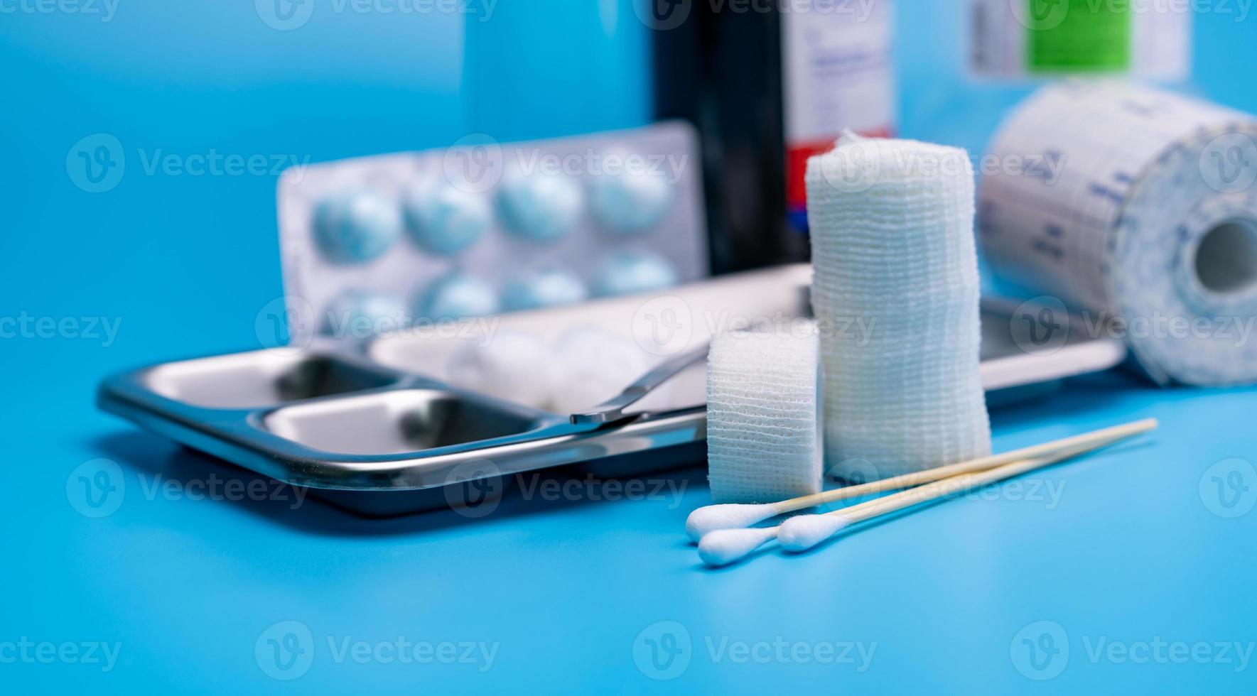 Wound care dressing set. Selective focus cotton stick and elastic cohesive retention bandage on blur stainless steel plate, forceps, conforming bandage, and cotton ball with alcohol. Medical supply. photo