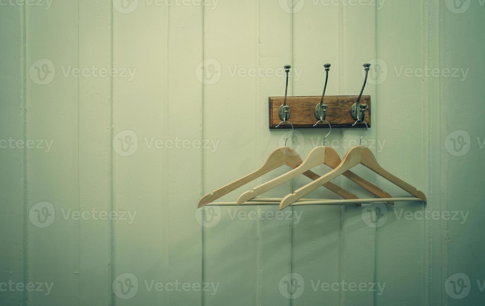 Brown wooden cloth hanger hanging on metal hook on white wooden wall background. Empty coat hanger in white vintage room. Hook install on wood wall with space for text. Rustic style fitting room. photo