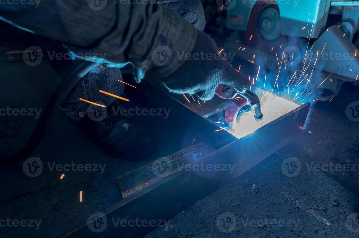 Welder welding metal with argon arc welding machine and has welding sparks. A man wears protective gloves. Safety in industrial workplace. Welder working with safety. Worker in steel industry factory. photo