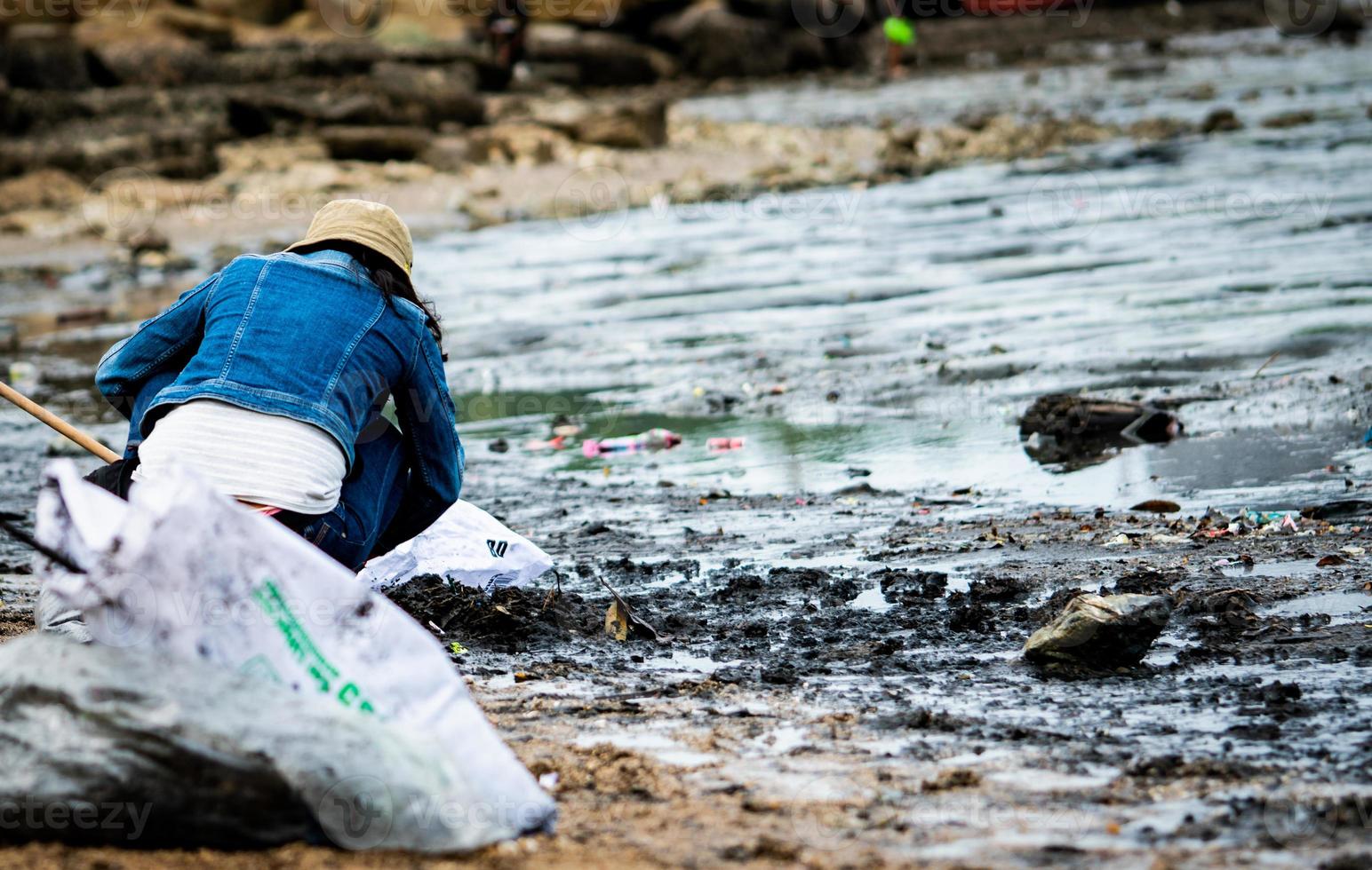 Volunteers sit and picking up garbage on the beach. Beach cleaner collecting garbage on the sea beach in to transparent plastic bag. Volunteers cleaning the beach. Tidying up rubbish on beach. photo