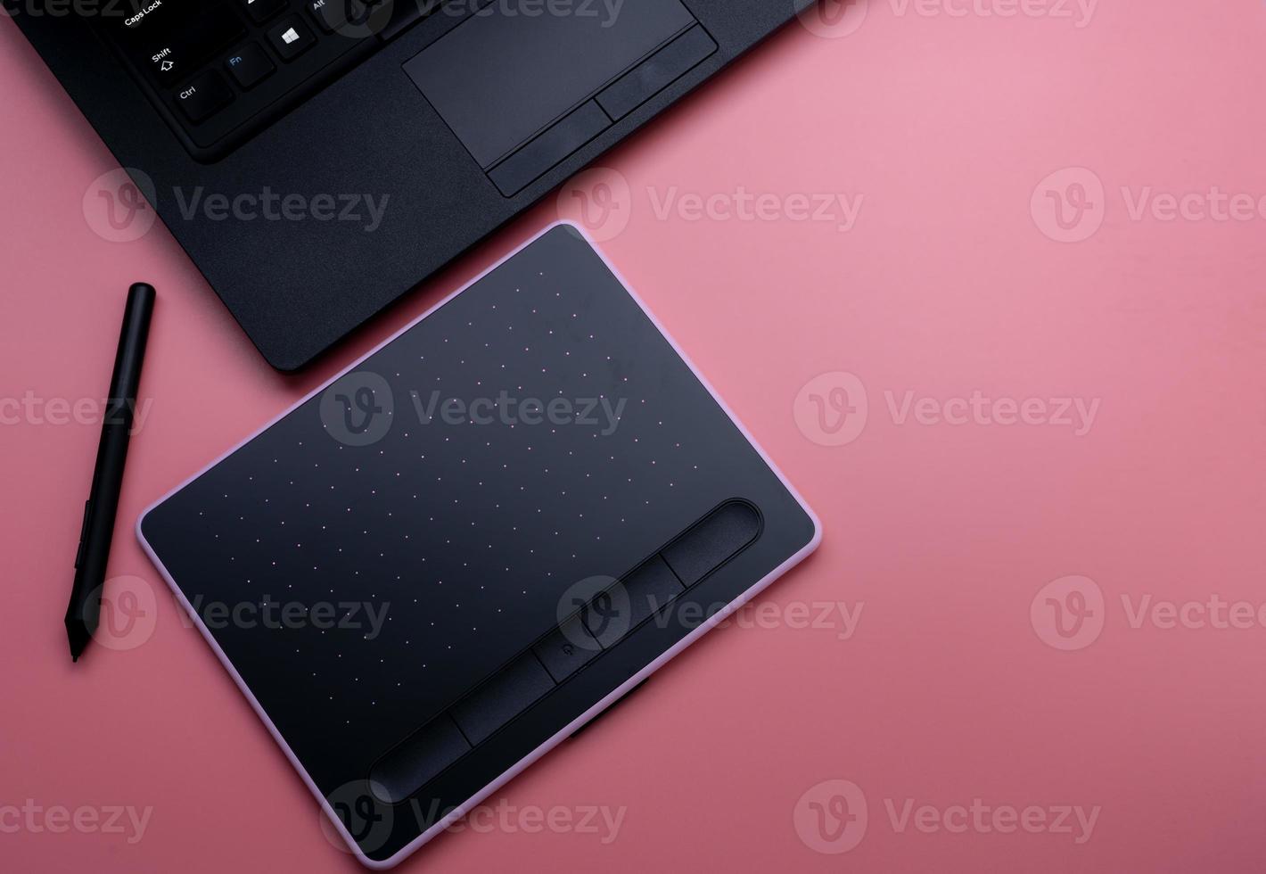 Top view of black pen mouse, digital tablet, and laptop for graphic design work on pink background. Above view of pen graphic tablet. Gadget for graphic designer. Bluetooth and wireless device. photo