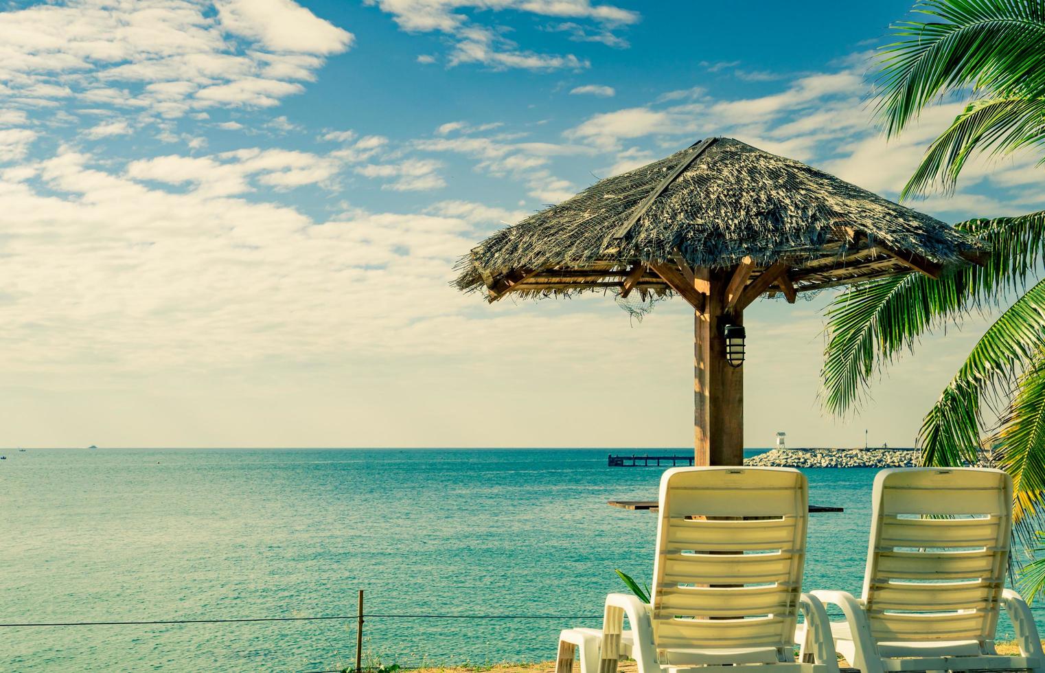 Tropical beach landscape with beach chairs and parasol on sand next to the sea on a beautiful sunny day. Scenic water and pier background at resort. Concept of summer vacation time of love couple. photo