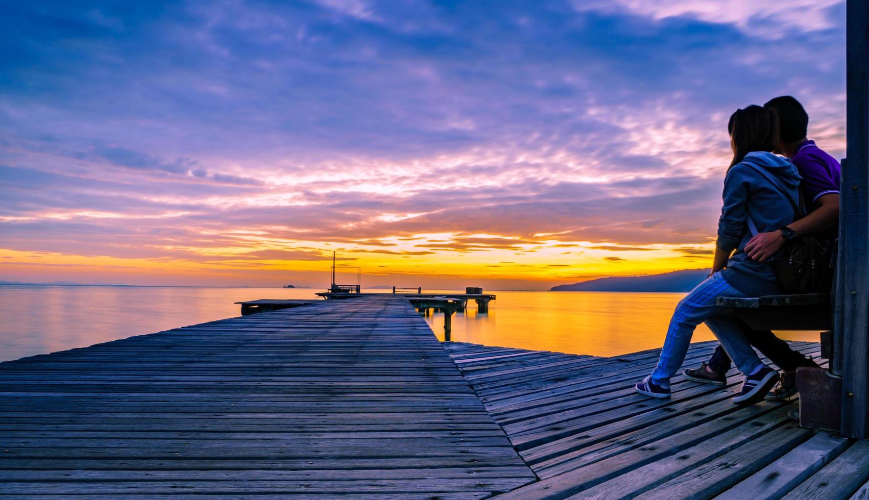 The romantic young couple is hugging on a wooden pier that stretched into the sea at sunrise and had a beautiful golden sky. photo