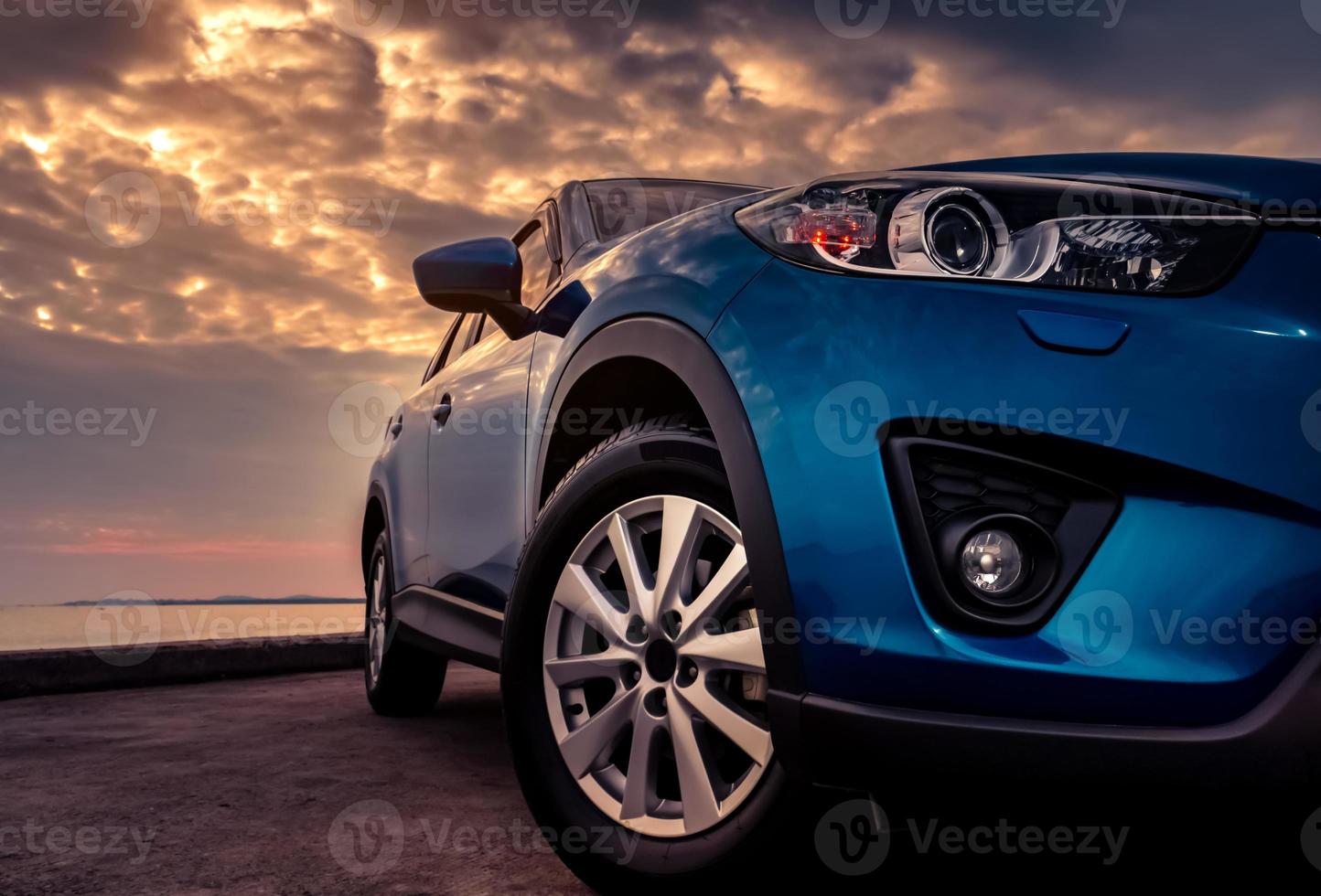 camión suv azul con diseño deportivo y moderno estacionado en una carretera de hormigón junto al mar al atardecer por la noche. concepto de tecnología de automóviles híbridos y eléctricos. industria automotriz. faro delantero y luz antiniebla. foto