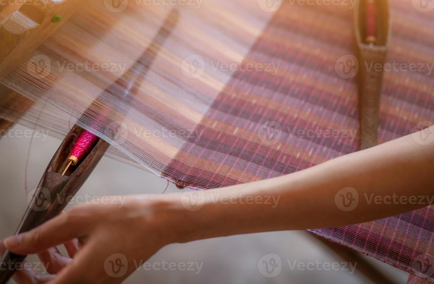 Woman working on weaving machine for weave handmade fabric. Textile weaving. Weaving using traditional hand weaving loom on cotton strands. Textile or cloth production in Thailand. Asian culture. photo