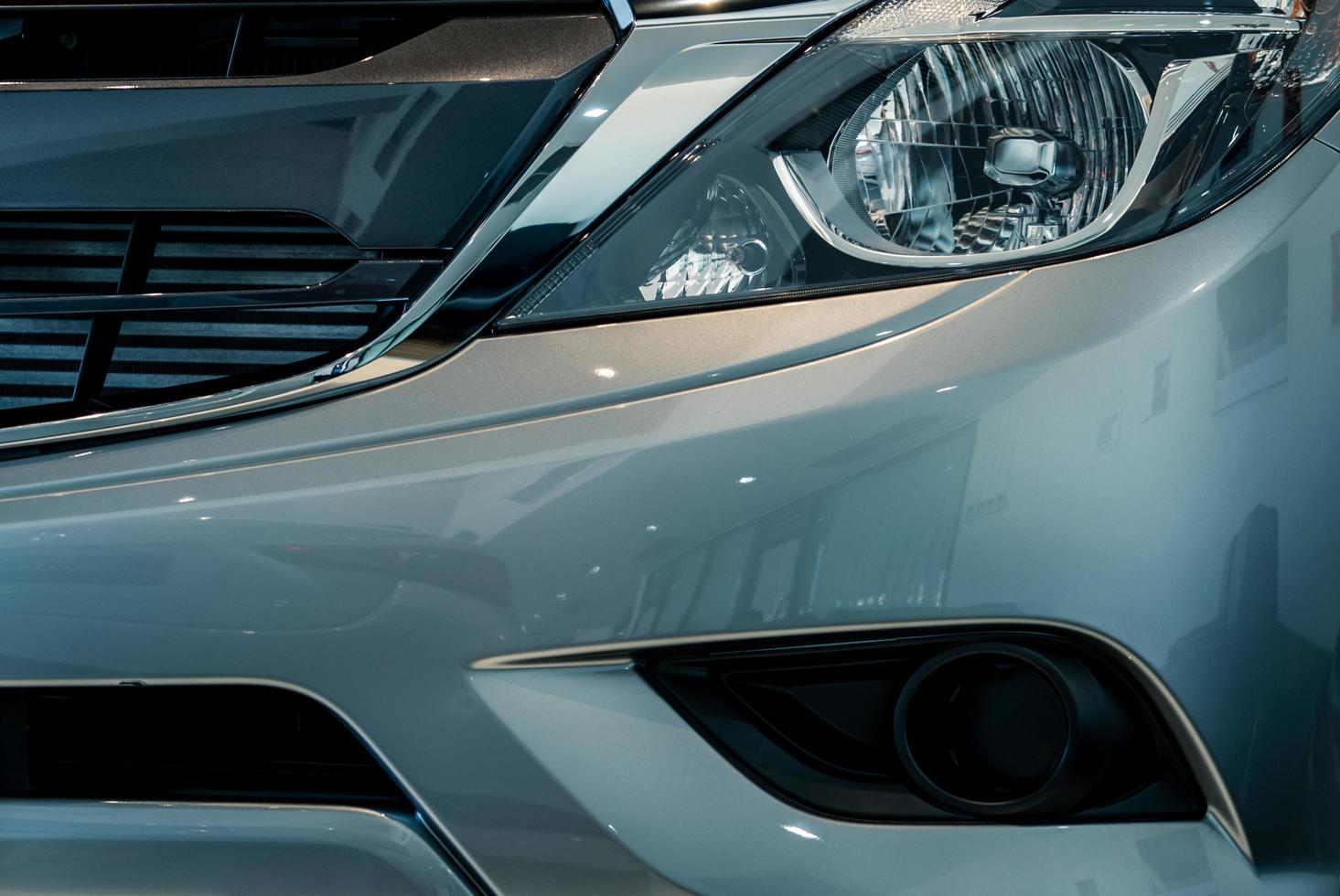 Closeup headlamp of gray SUV car parked in modern showroom. Shiny new car with reflection of modern showroom. Automotive industry. Electric car technology. Automobile headlight. Car dealership concept photo