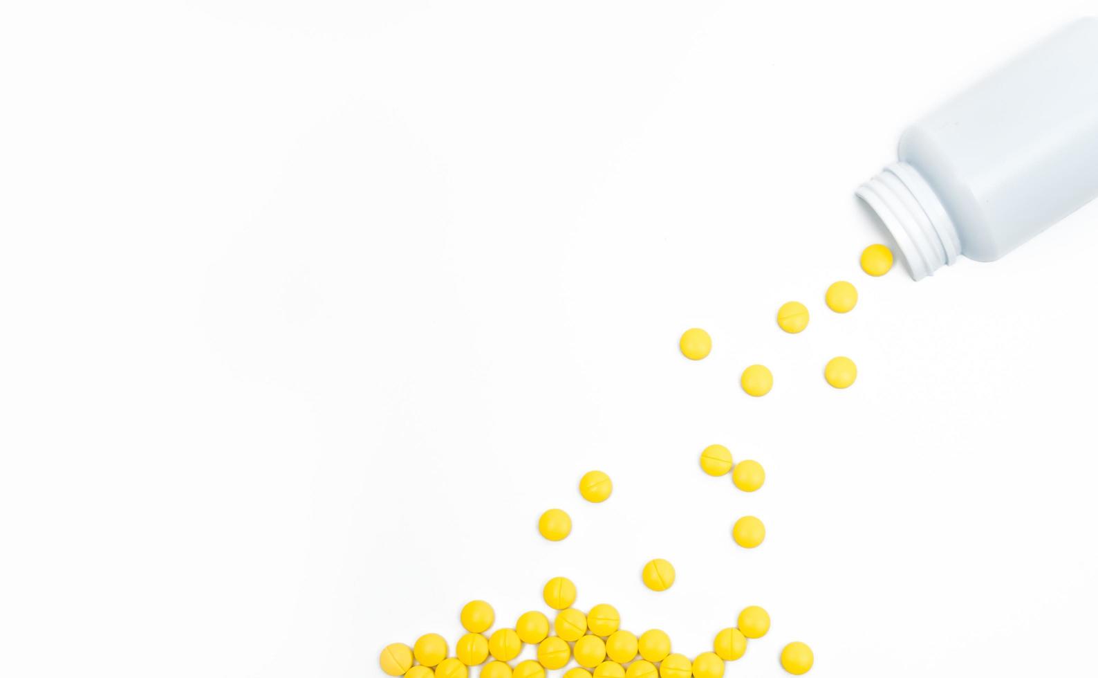Yellow film coated tablets pills spilling out of pill bottle on white background with copy space. Painkiller tablet pills. NSAIDs pills for muscle pain. photo