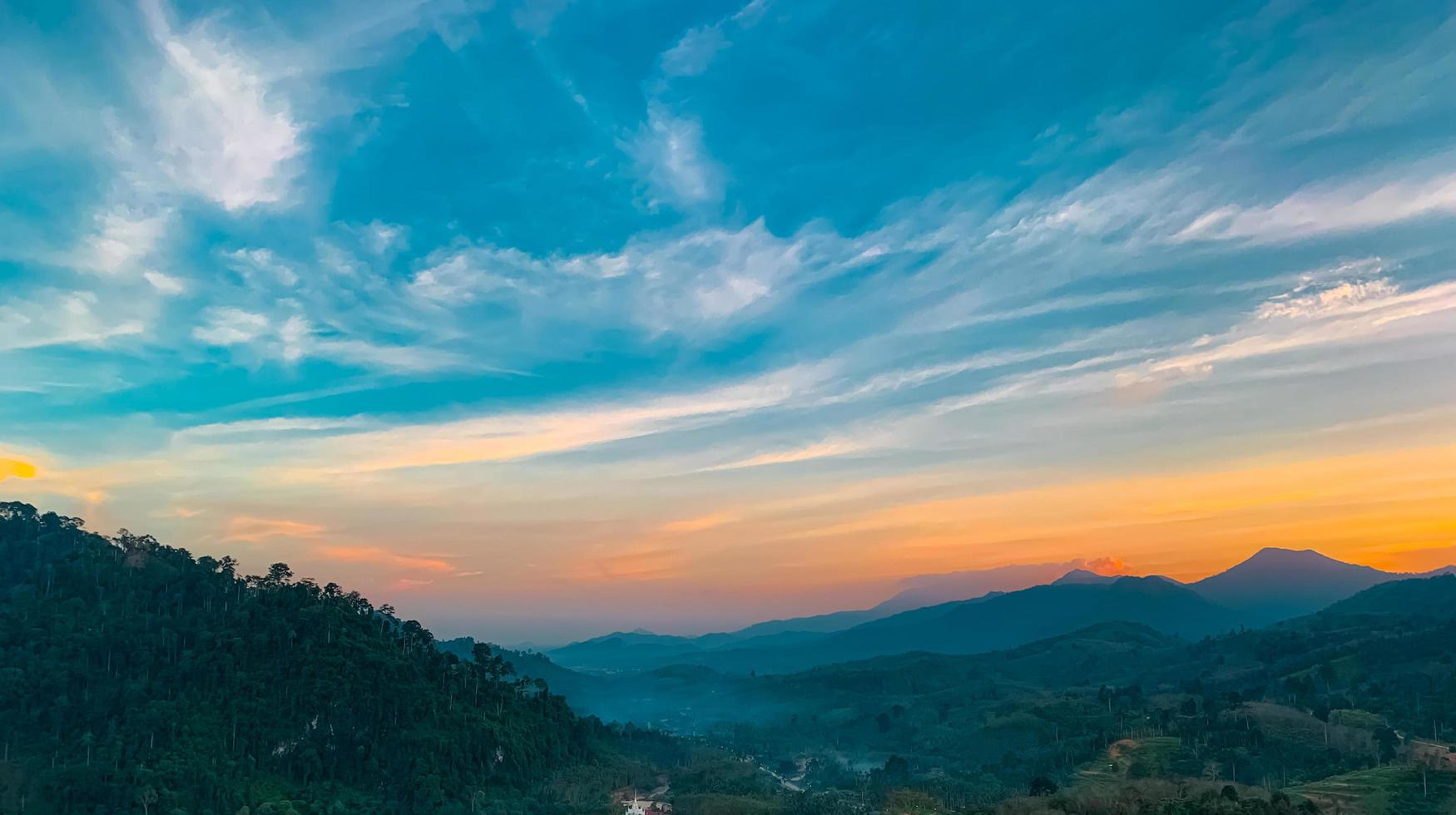 Beautiful nature landscape of mountain range with sunset sky and clouds. Rural village in mountain valley in Thailand. Scenery of mountain layer at dusk. Tropical forest. Natural background. photo