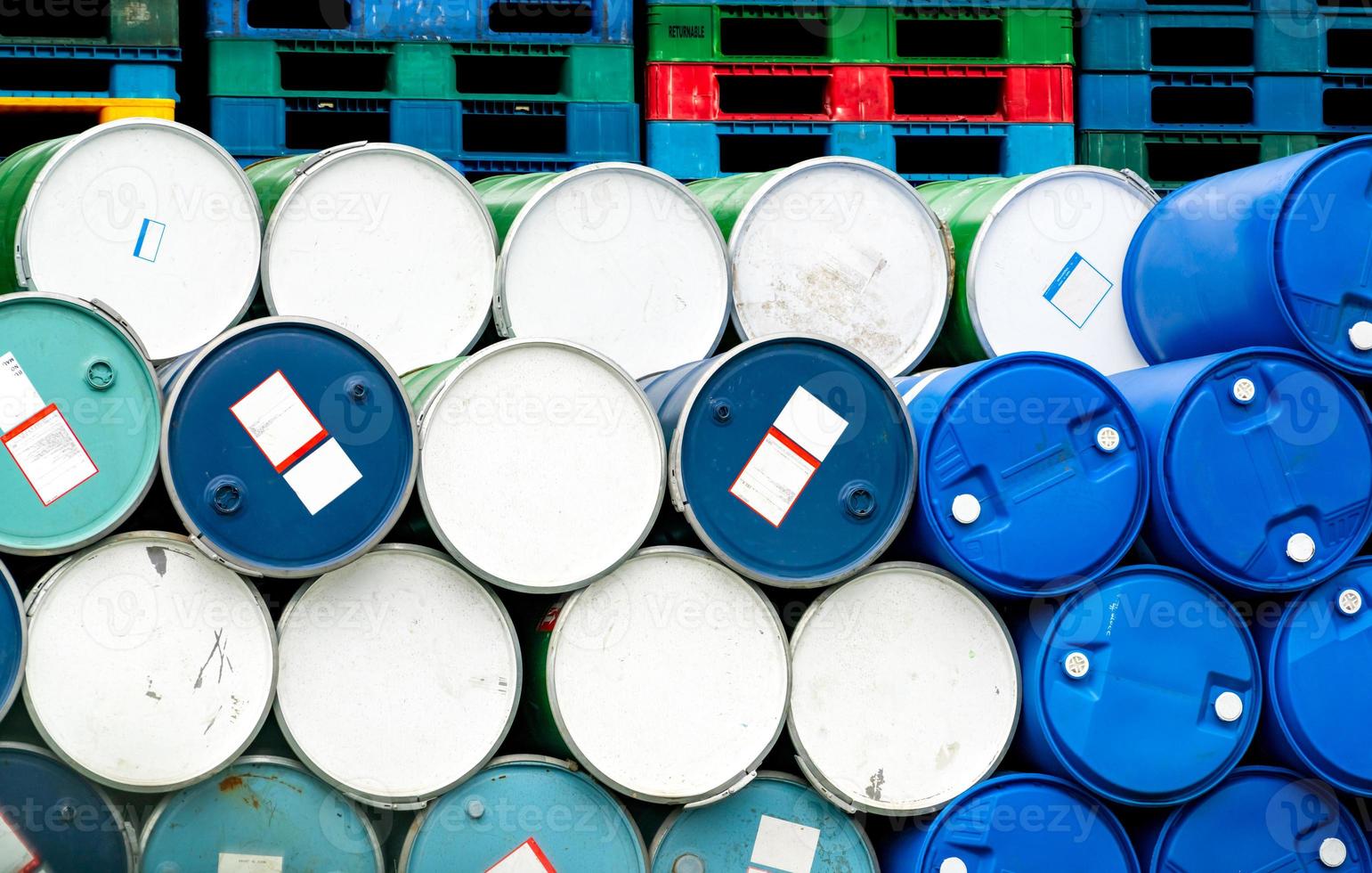 Old chemical barrels in front of stacked plastic pallet at the factory. Blue and green oil drum. Steel and plastic oil tank. Toxic waste warehouse. Hazard chemical barrel. Industrial waste in drums. photo