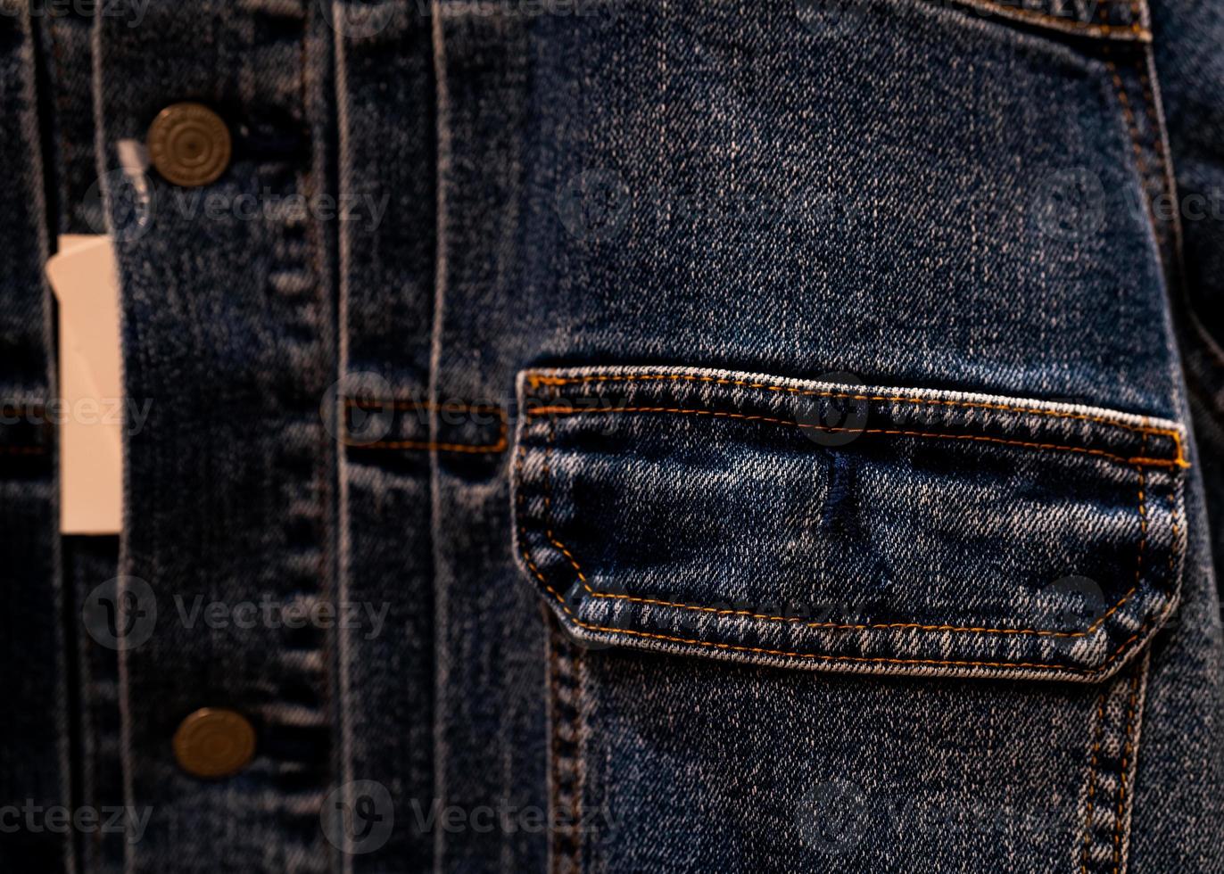 Selective focus on denim jean jacket pocket in clothes shop. Denim jacket pocket texture background. Textile industry. Jeans fashion and shopping concept. Clothing concept. Denim jacket for sale. photo