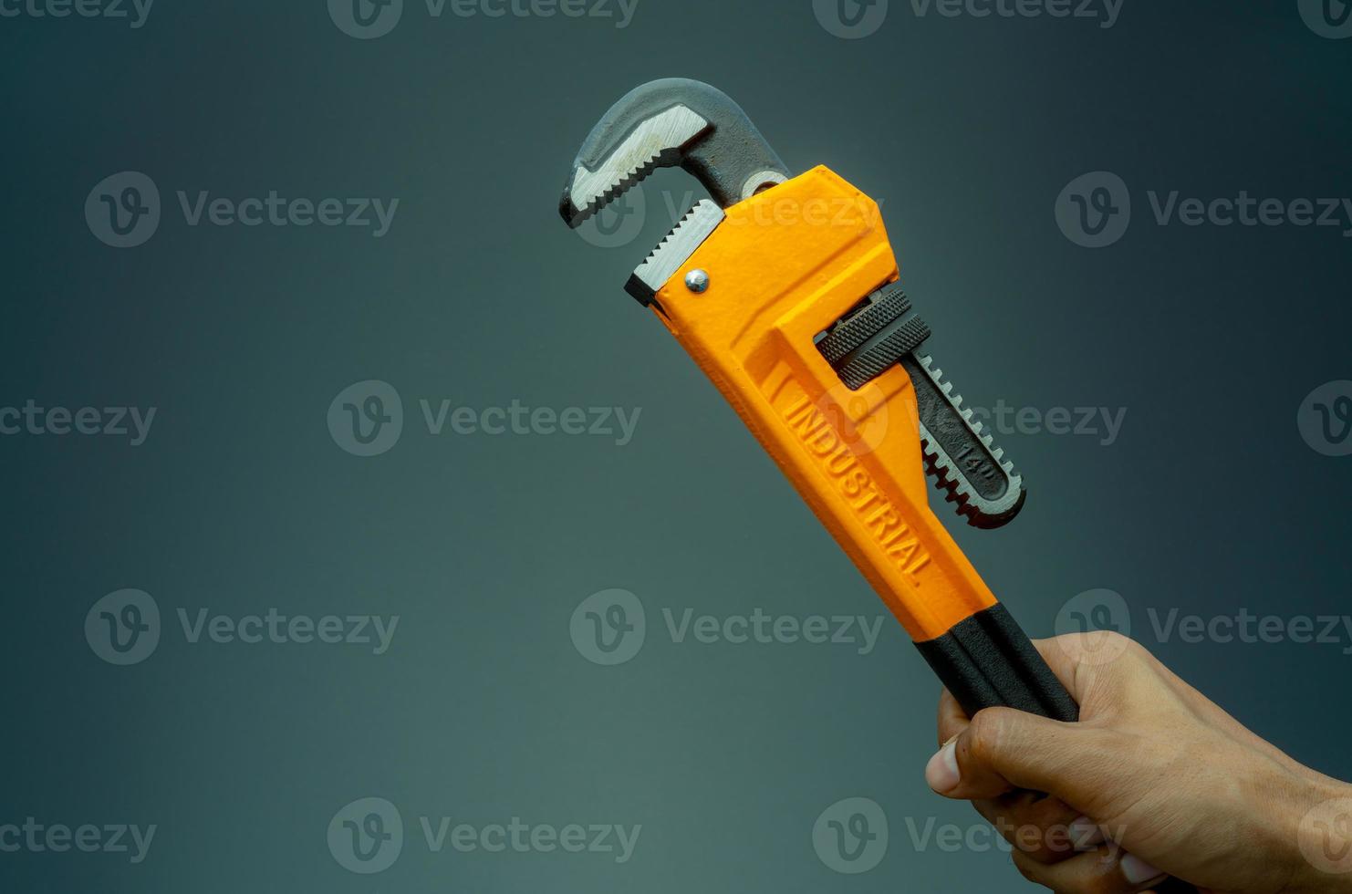 Plumber hand holding handle of chrome pipe wrench isolated on dark background. Metal monkey wrench for plumber. Mechanic tools. Hardware for fix and maintenance service. Clamping tools for plumbing. photo