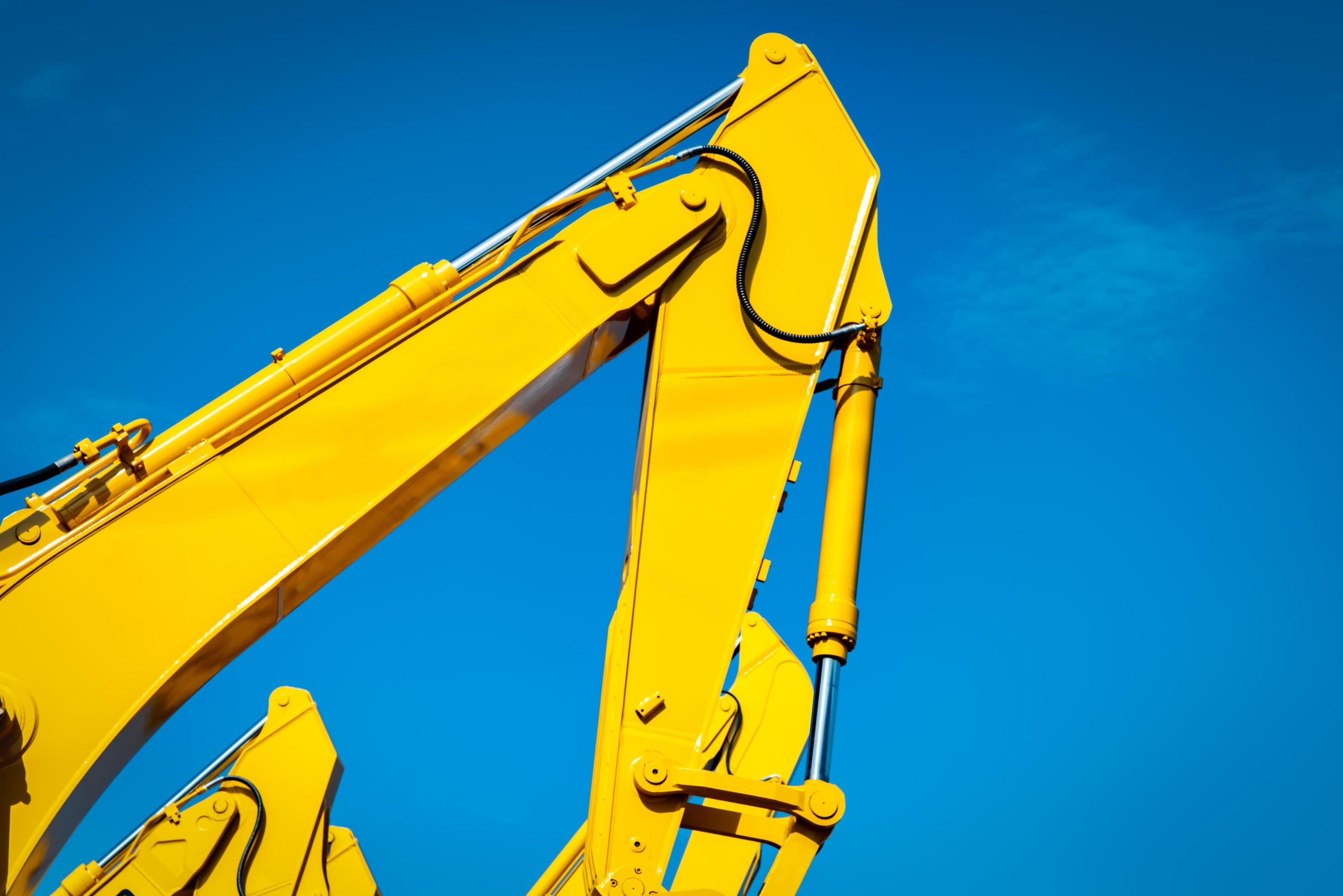 Yellow backhoe with hydraulic piston arm against clear blue sky. Heavy