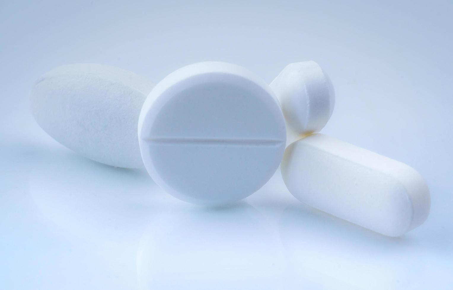 Round and oval white tablets pills on whit background. Selective focus on white tablets pills. Pharmaceutical industry. Drug production. Pharmacy drugstore products. Pharmaceutical manufacturing. photo