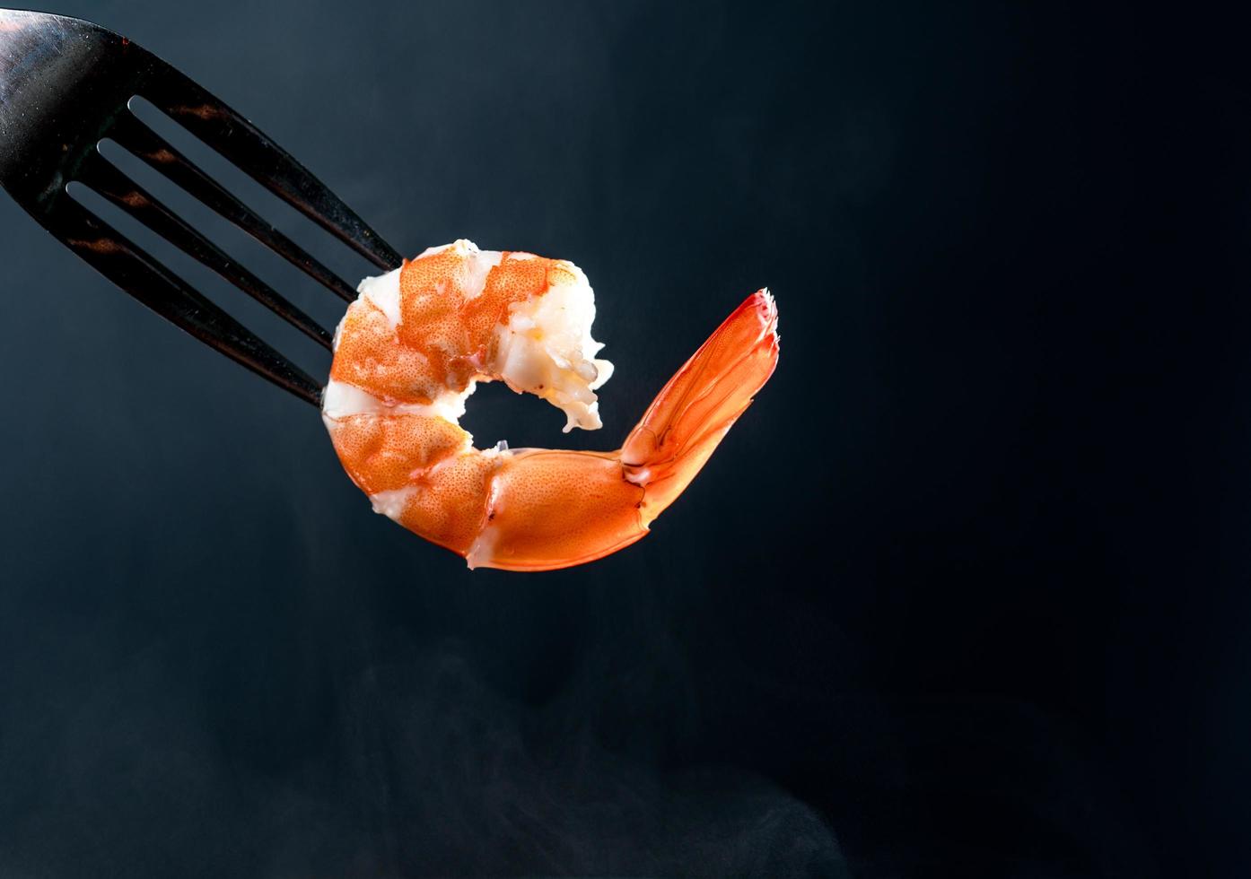 Steamed shrimp on fork isolated on dark background with copy space. Seafood buffet in restaurant concept. Use for seafood buffet promotions advertising photo