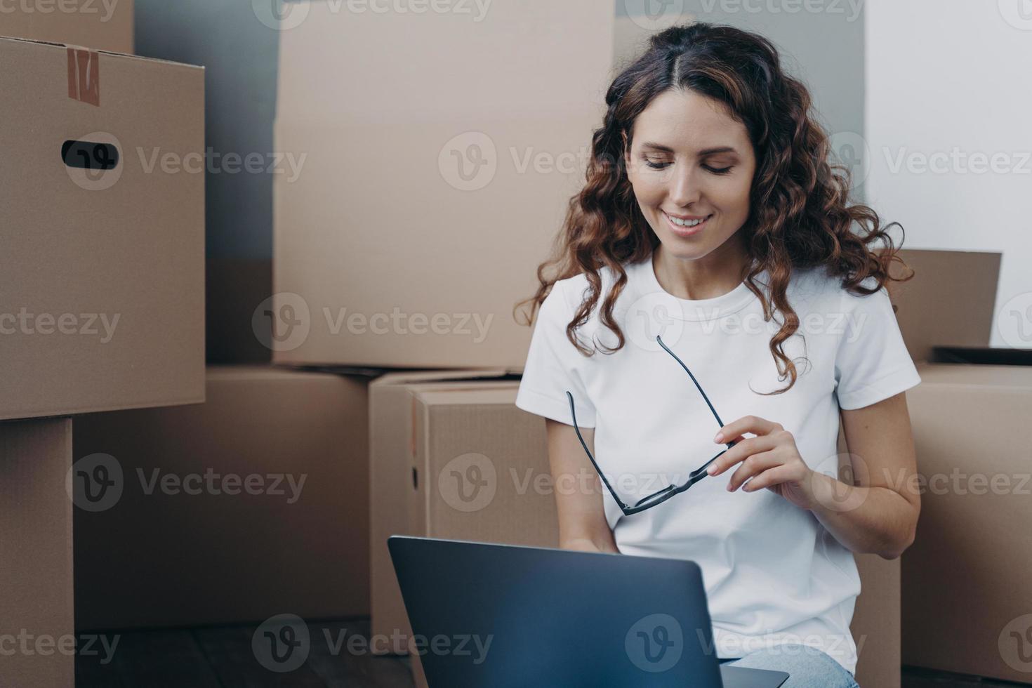 la chica española está sentada en el suelo con un portátil antes de salir del apartamento. trabajo a distancia y freelance. foto