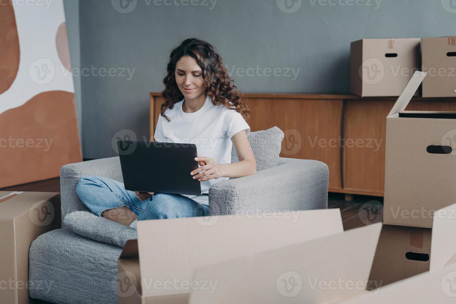 Happy lady is sitting in armchair and working with pc. Delivery service ordering through internet. photo