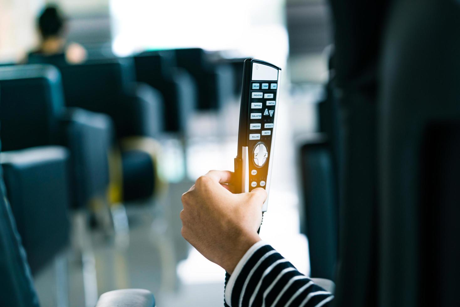 Asian woman use hand hold and press button on remote to control robotic massage chairs to relax head, shoulders, and back after work hard all day photo