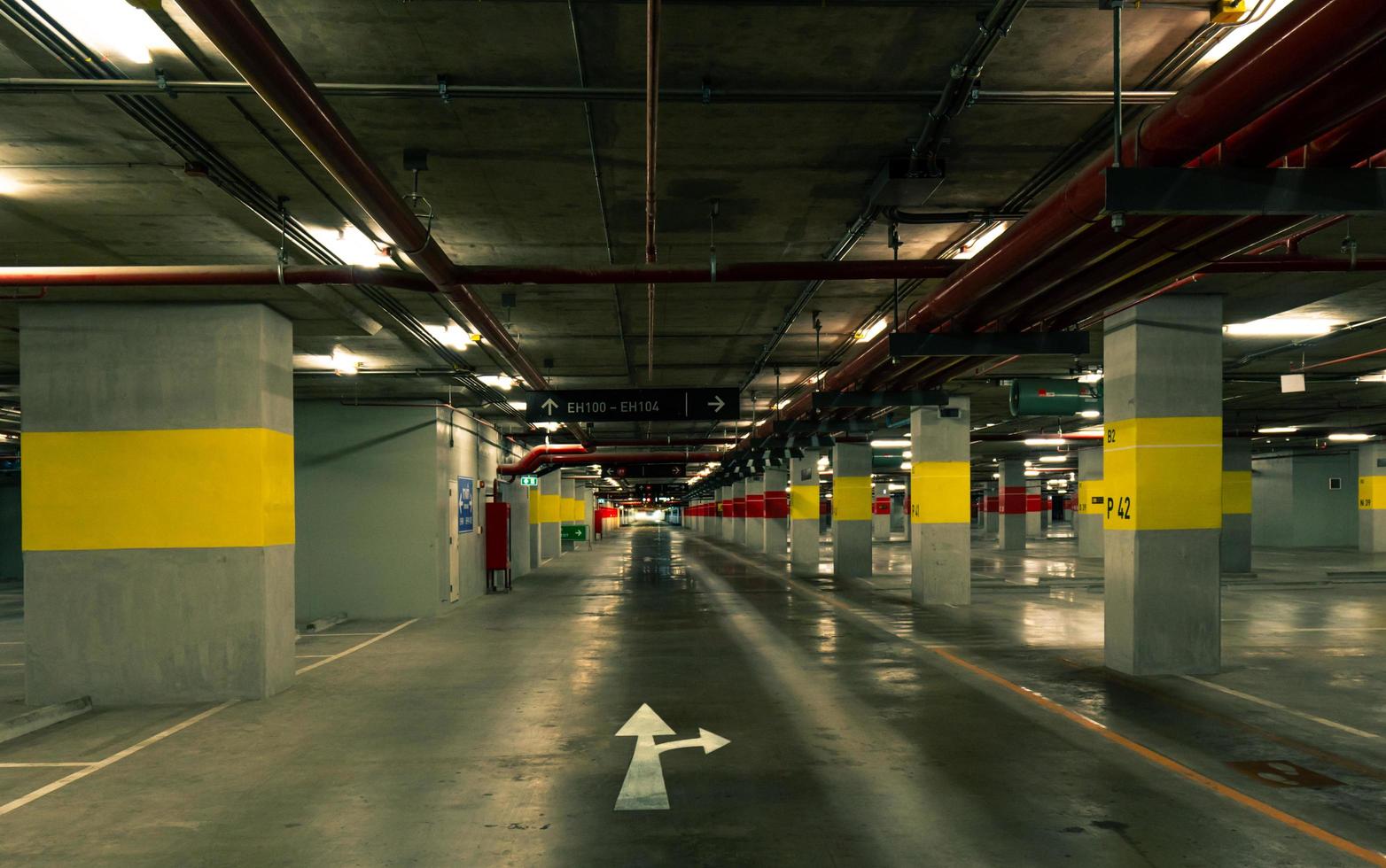 vista en perspectiva del aparcamiento interior vacío en el centro comercial. garaje subterráneo de hormigón con lámpara abierta por la noche. señal de dirección blanca. elige la manera de vivir tu vida. cableado y fontanería. foto