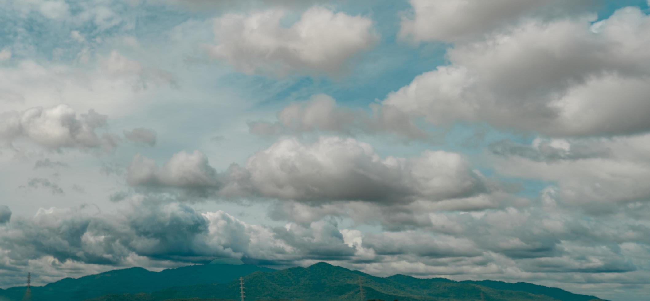 Panorama view of the overcast sky above the green mountain and electric pylons. Dramatic sky and cumulus clouds. Cloudy and moody sky. Storm sky. Cloudscape. Overcast clouds. Beauty in nature. photo