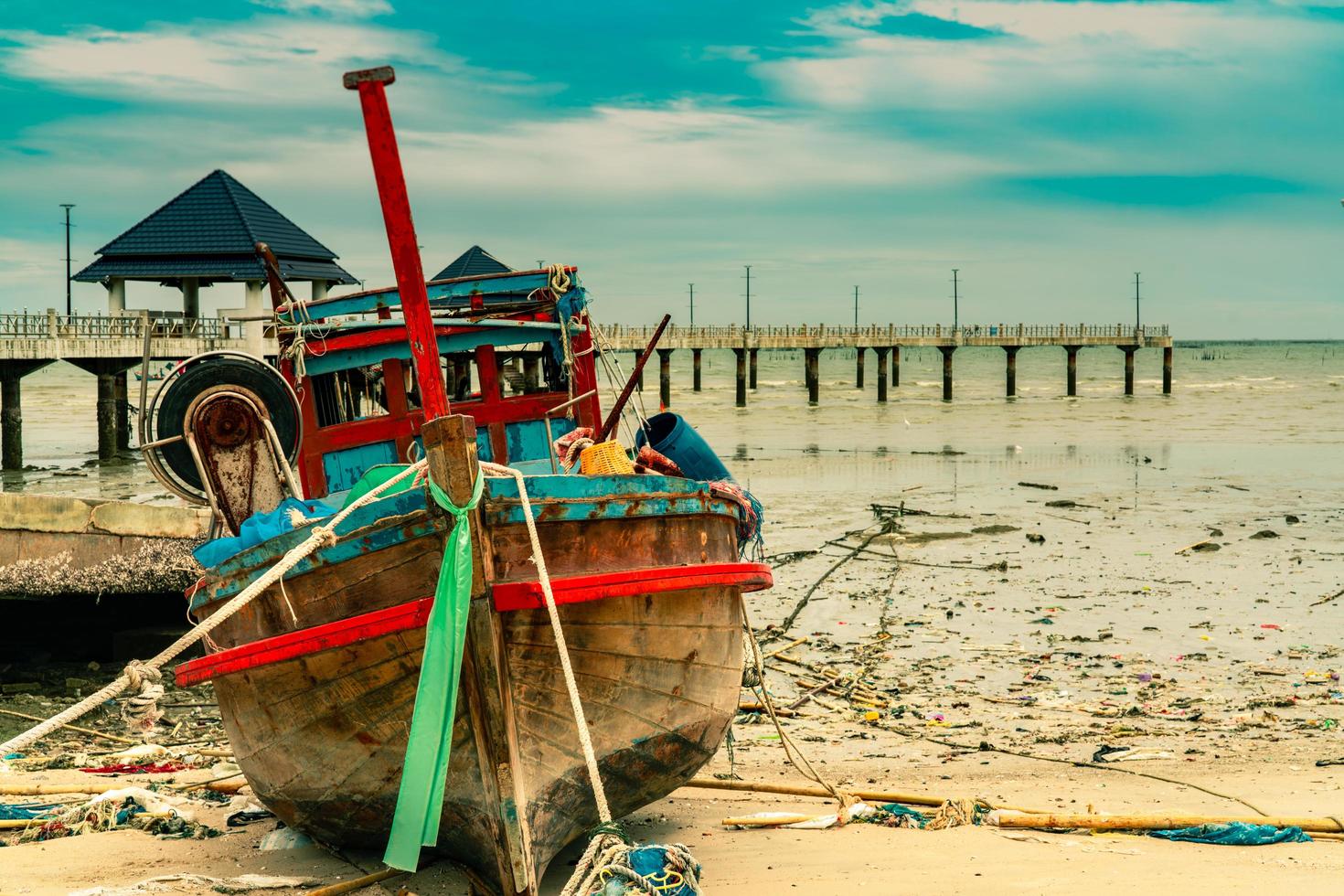Fishing boat on sand beach near the bridge and sea. Relaxation on paradise tropical beach and resort concept. Garbage on the beach. Coastal environmental pollution. Marine environmental problems. photo