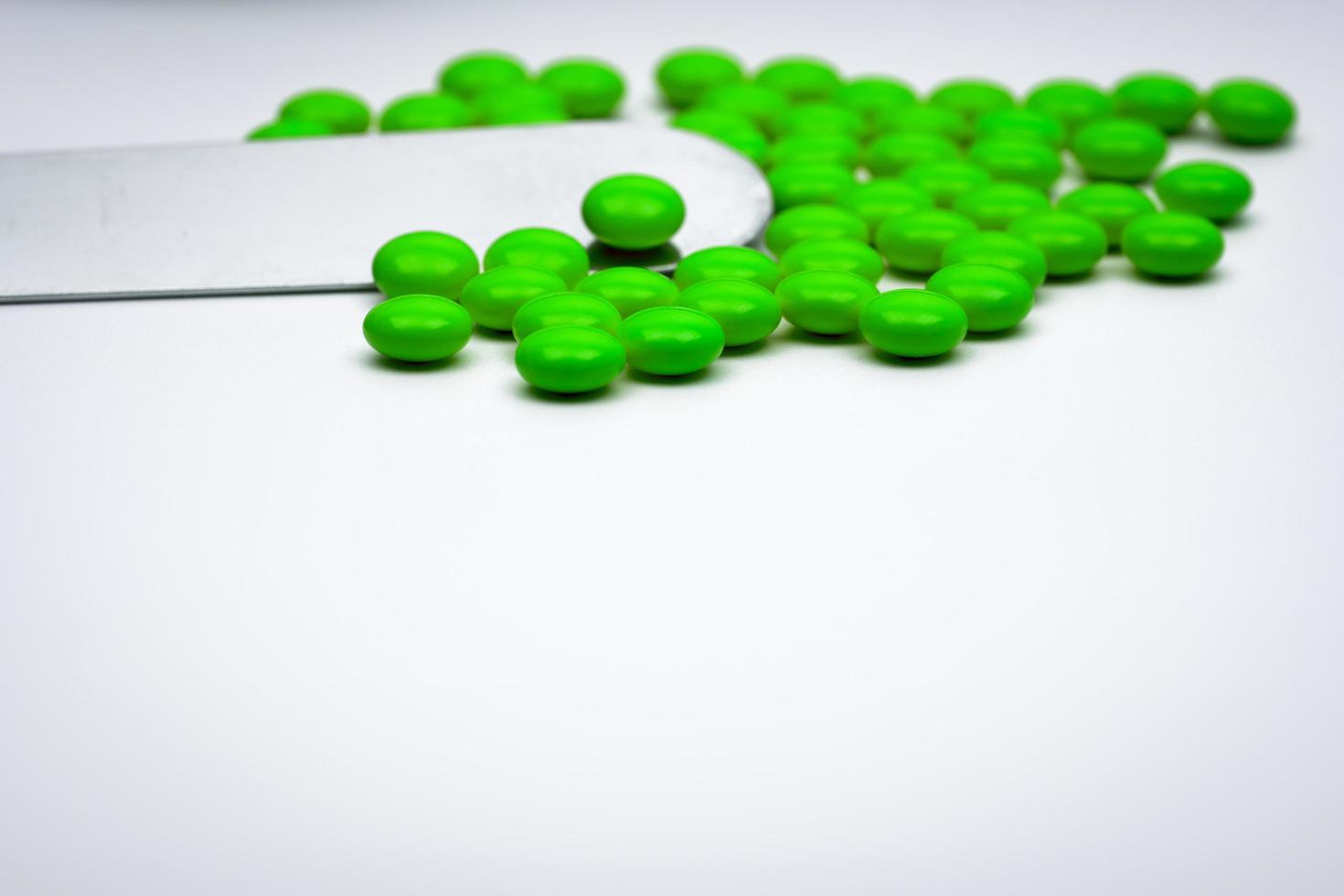 Selective focus of green round sugar coated tablets pills and stainless steel spatula on white background with copy space photo