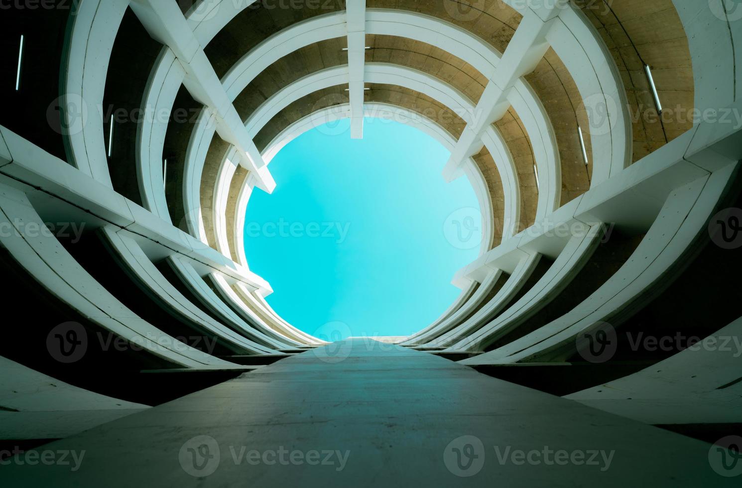 edificio de estacionamiento de varios pisos con vista inferior con vista al cielo azul en el centro. arquitectura del edificio de la curva espiral. garaje de estacionamiento de varios niveles. estacionamiento interior para automóviles con luz de lámpara instalada en el techo. foto