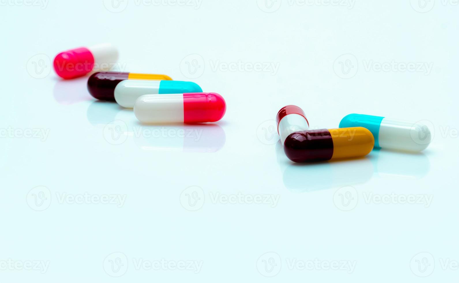 Multi-color antibiotic capsule pills spread on white background. Antibiotic drug resistance. Antimicrobial capsule pills. Pharmaceutical industry. Pink, white, blue, yellow, and red capsule pills. photo